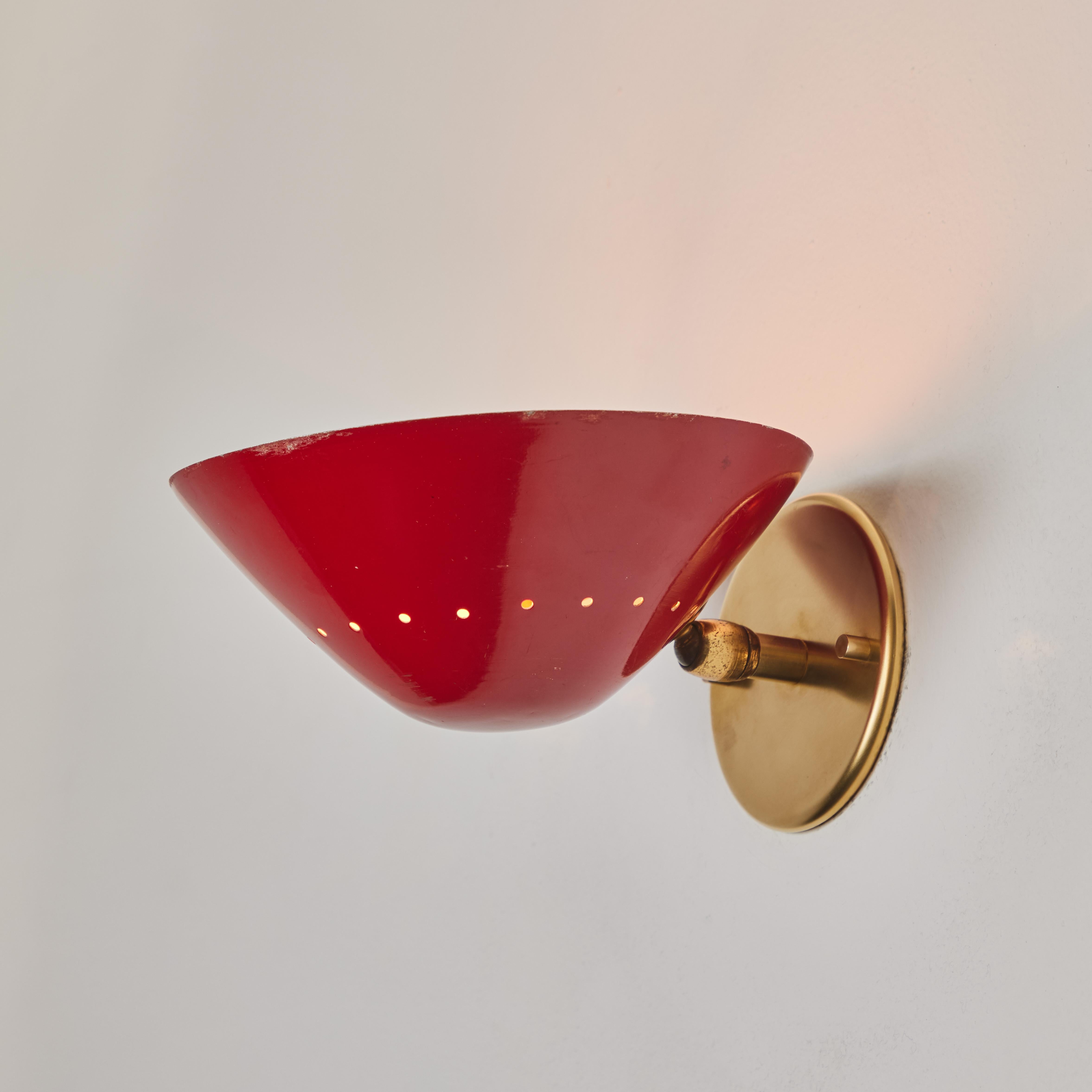 Applique murale perforée Stilnovo des années 1950, de couleur rouge. Abat-jour en métal peint en rouge avec quincaillerie en laiton patiné et intérieur peint en blanc. Cette lampe murale très fonctionnelle peut être montée vers le haut ou vers le