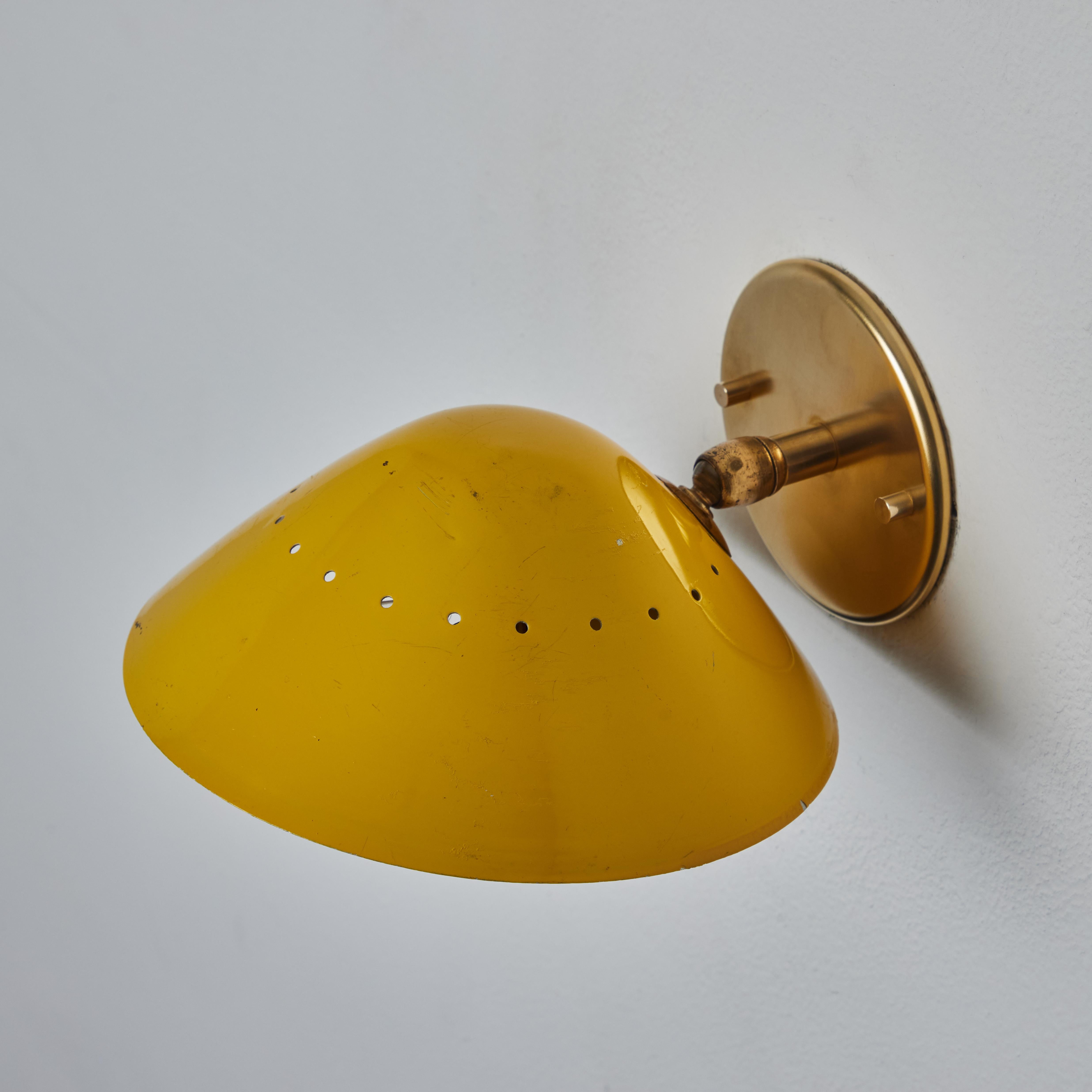 1950s Stilnovo perforated wall sconce in yellow. Executed in yellow painted metal shade with patinated brass hardware and white painted interior. This highly functional wall lamp can be mounted as either upward or downward-facing. Its swivel-mounted