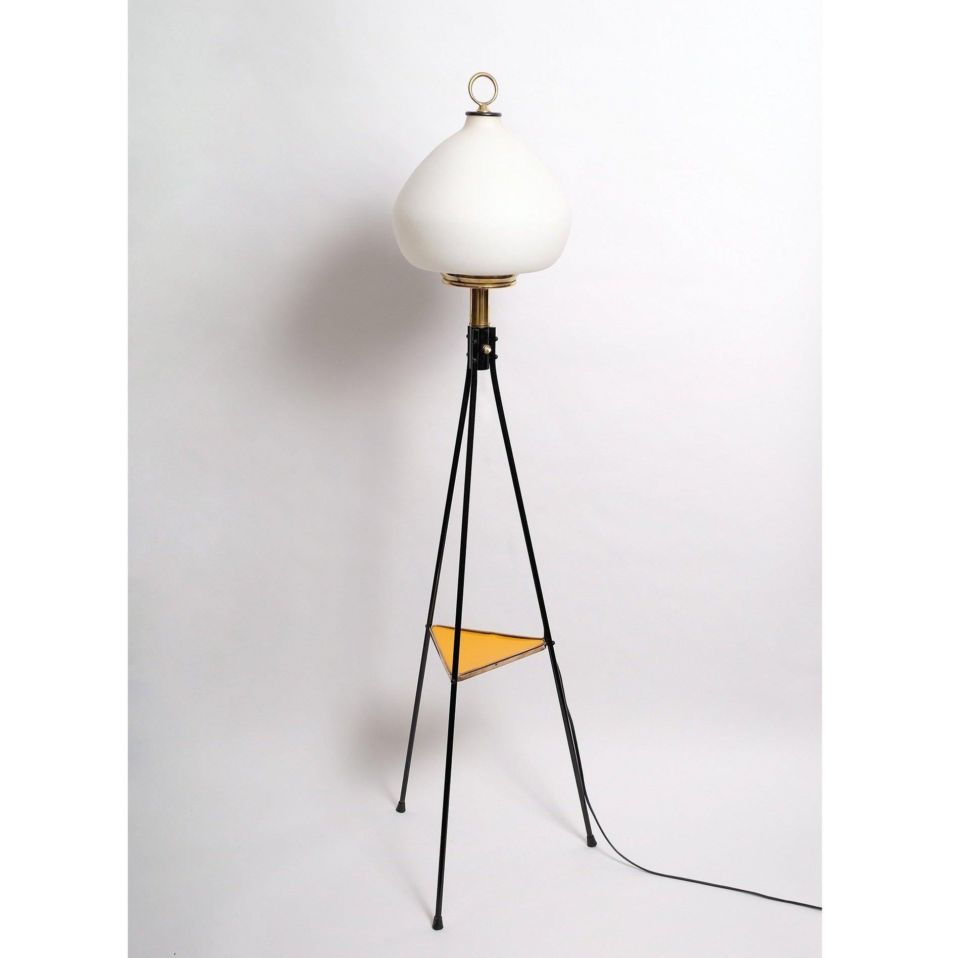 Stilnovo tripod floor lamp, Italy, 1950s.  Lacquered steel legs, brass framed yellow laminate mid-level shelf, brass body and cased opaline glass shade in mint condition.  40 to 60 watt E-26 Edison medium base incandescent bulb or higher if LED/CFL.