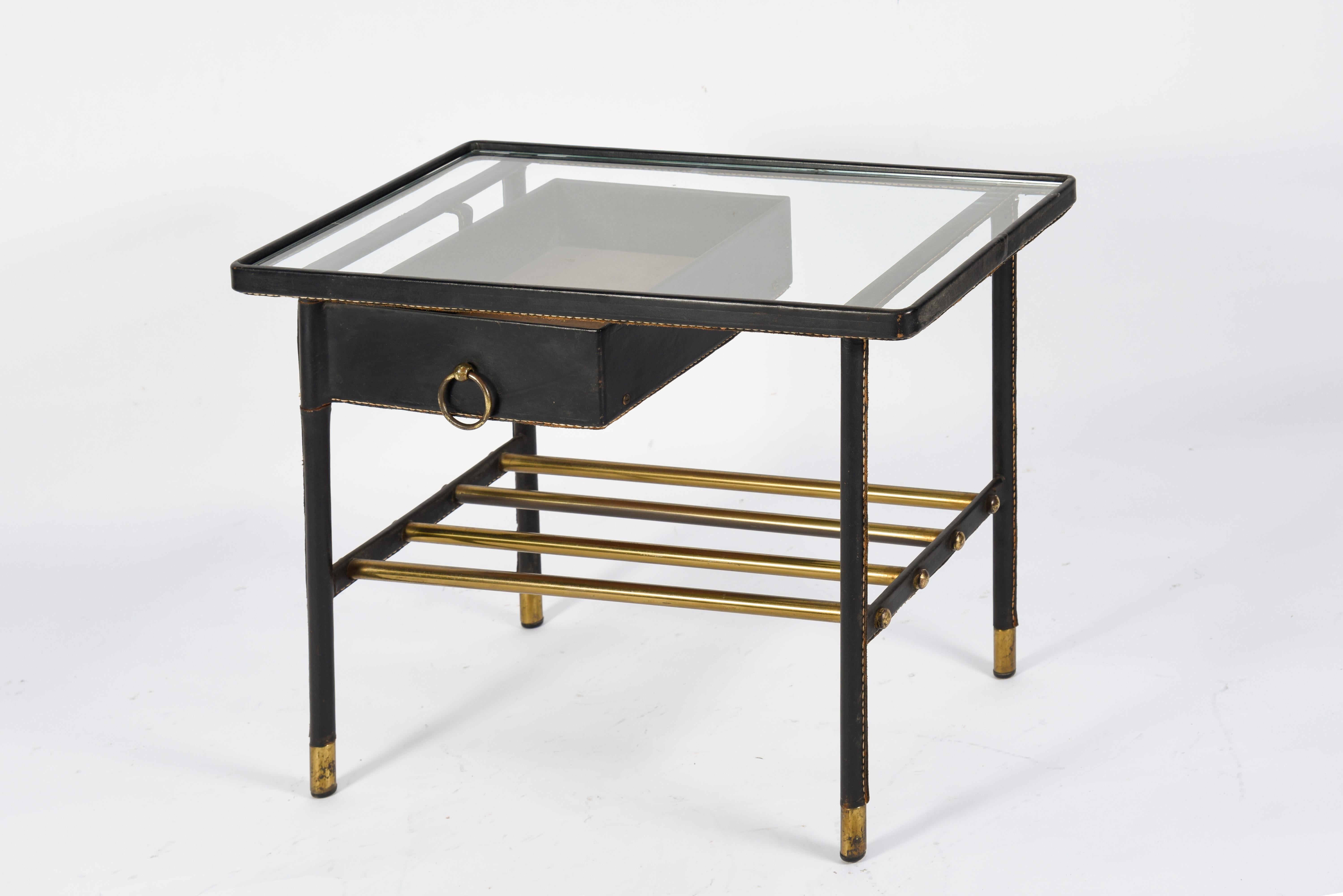 Incredible black leather side table by Jacques Adnet with signature saddle stitched bamboo legs, original glass top and brass loop hardware detailing.
Single drawer pivots with circular brass hardware.
Manufactured by 
