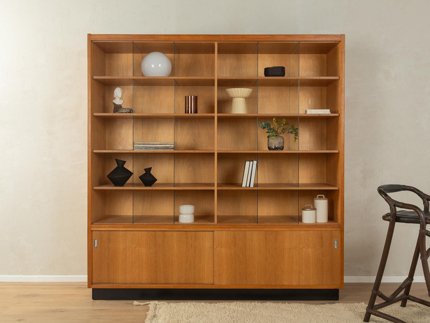 Armadio unico degli anni '50 proveniente da un'ex merceria. Corpo di alta qualità impiallacciato in Oak con dieci ripiani, molti scomparti con divisori in vetro, due ante scorrevoli e una base nera a contrasto.

Caratteristiche di qualità:
buona