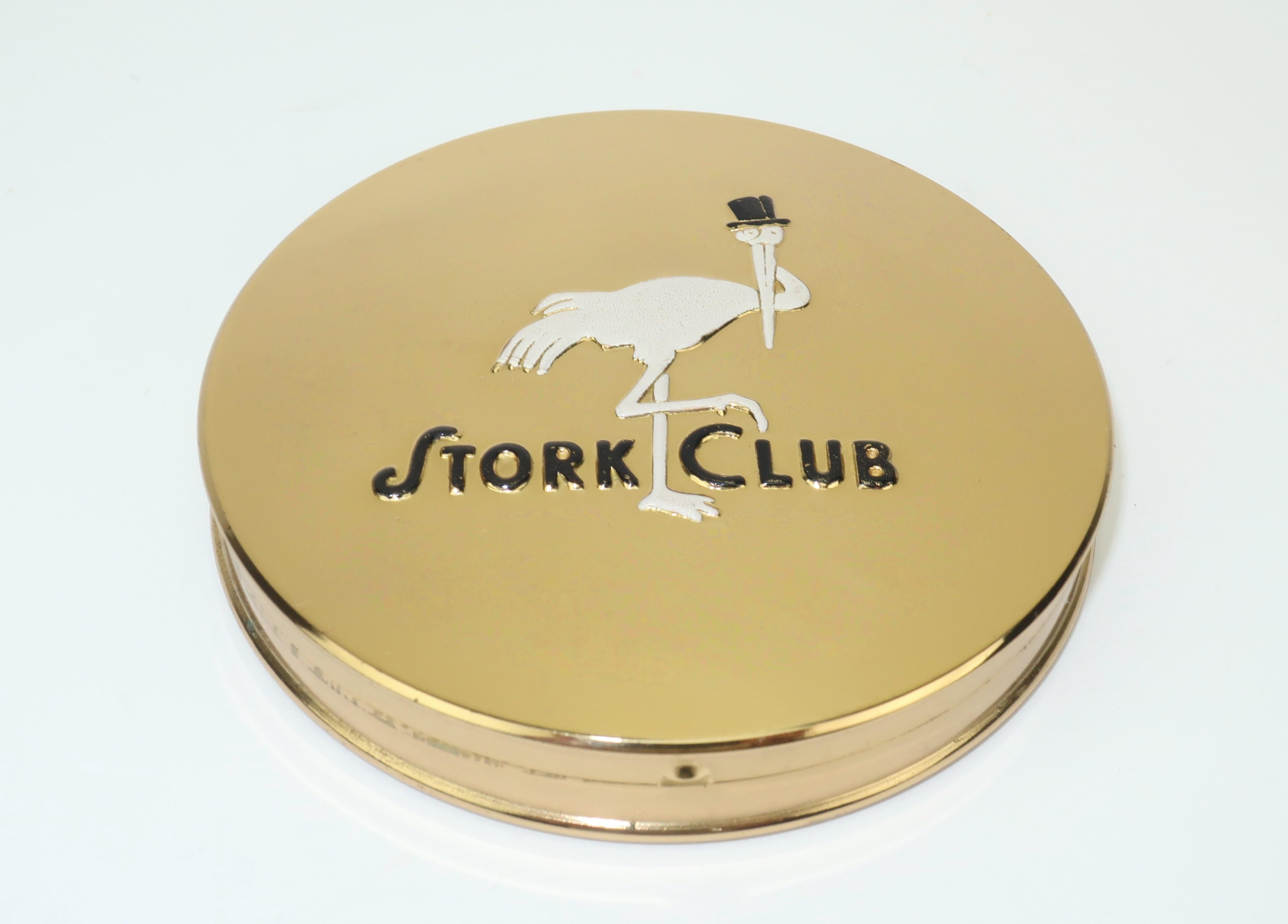 Own a piece of New York history with a souvenir gold tone powder compact from the famed Stork Club of Manhattan.  The compact displays the iconic art deco Stork Club logo in black and white enamel and the mirrored interior holds unused compressed