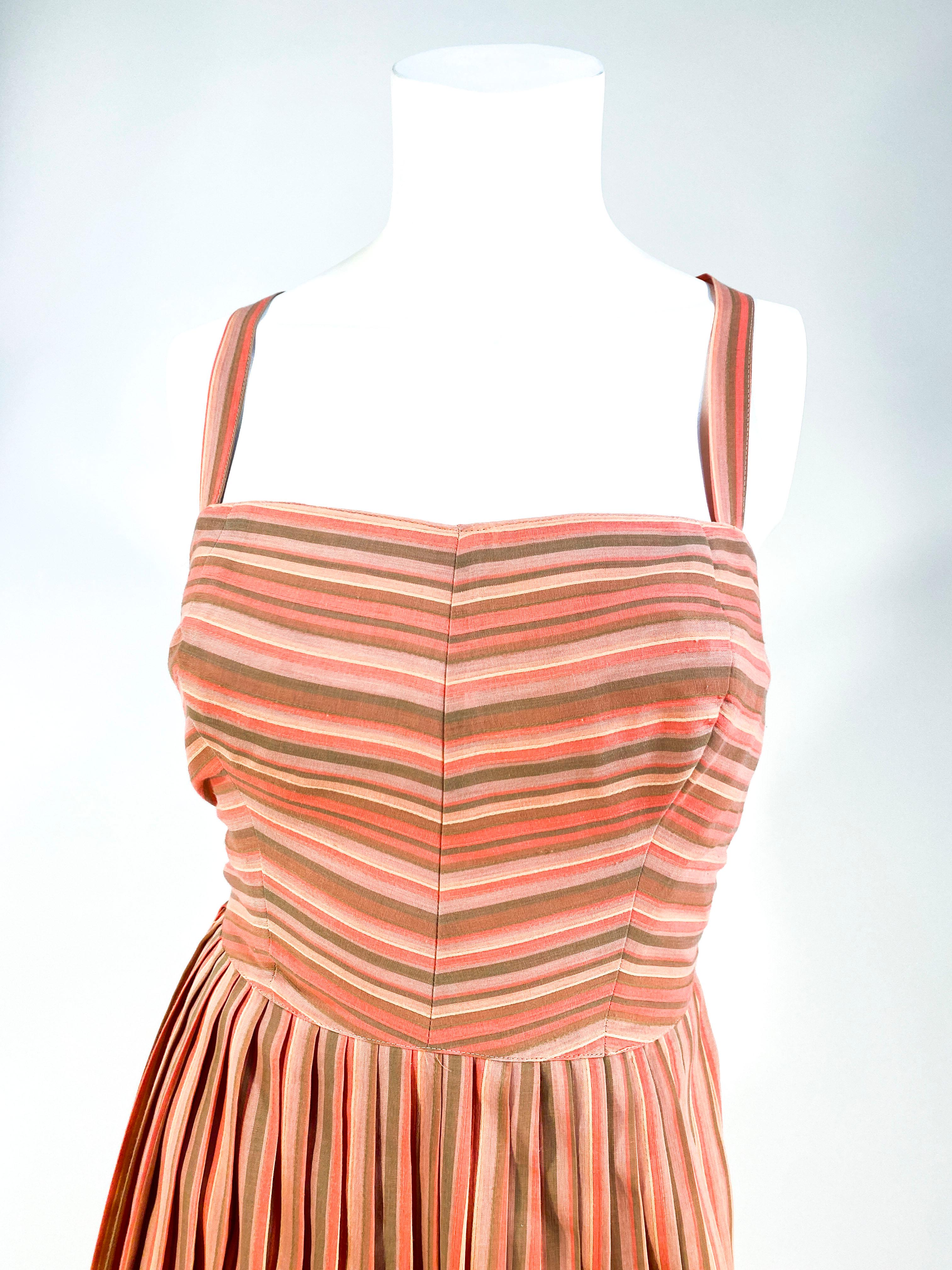 1950s cotton sunsuit featuring a narrow pattern-matched striped print (in soft cream, tan, peach and brown). The knife pleated overskirt hides the pantalettes with elastic leg openings. The straps are buttoned and are adjustable also the ruched back