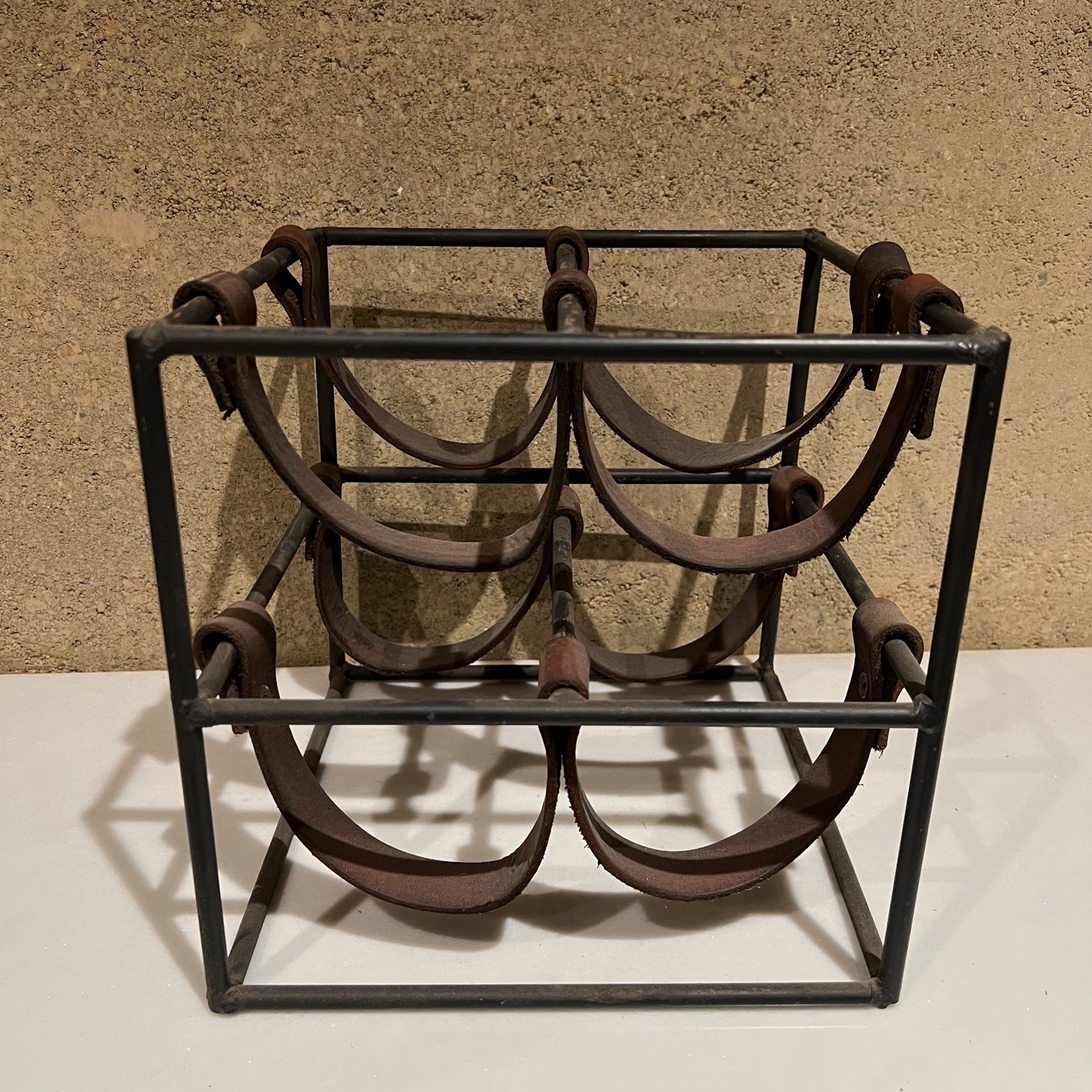 Leather wine holder rack.
1950s Mid-Century Modern style Arthur Umanoff vintage wine rack iron with leather straps
Features leather loops suspended between iron bars accommodates 4 bottles.
Unmarked.
Measures: 9.25 tall x 9.5 wide x 9.5