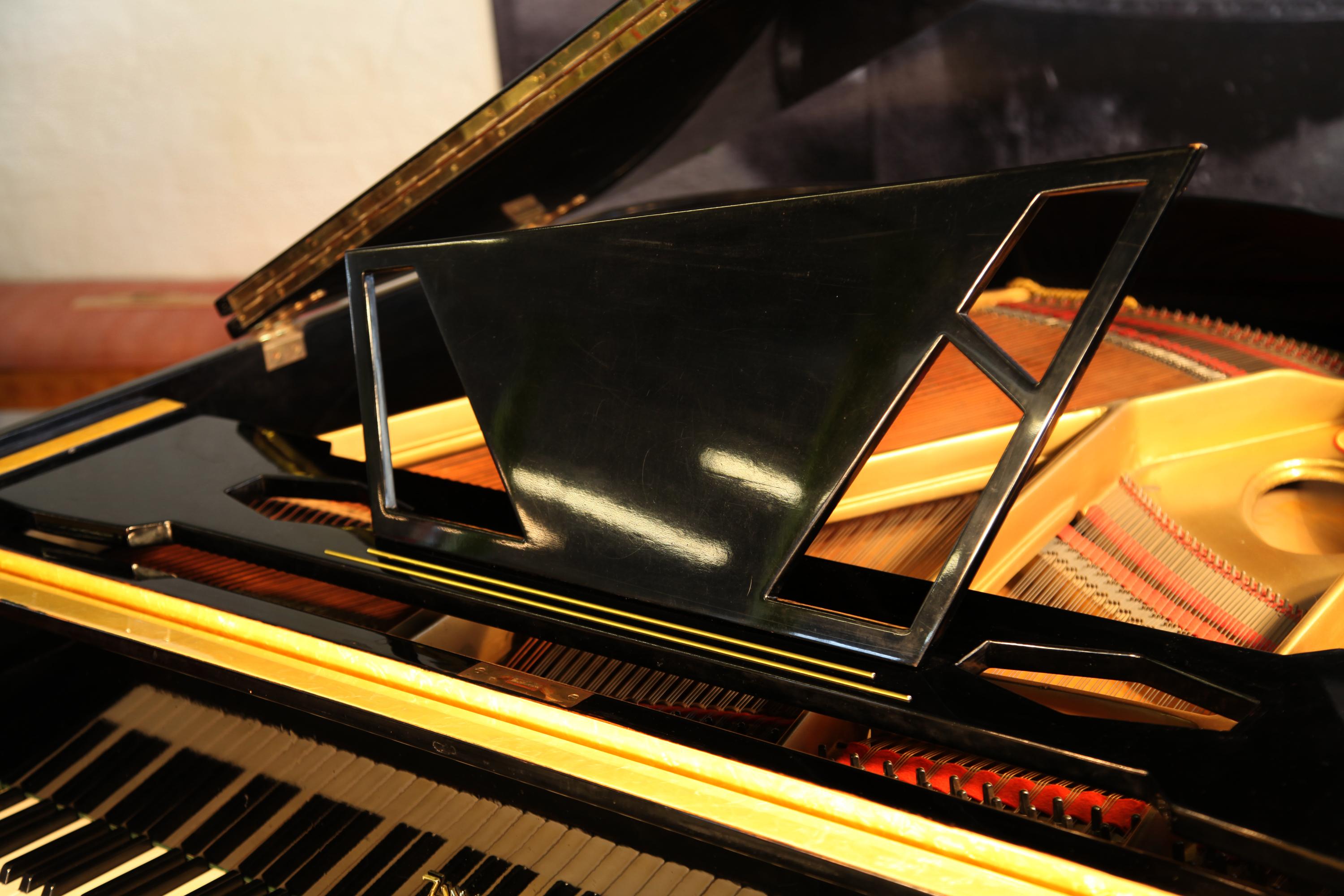 A 1950s style, Zimmermann baby grand piano with a contrasting black and yellow formica case. Piano features an asymmetrical music desk with geometric cut-outs. 
Angular styling is seen throughout the cabinet design. The tapered geometric legs are