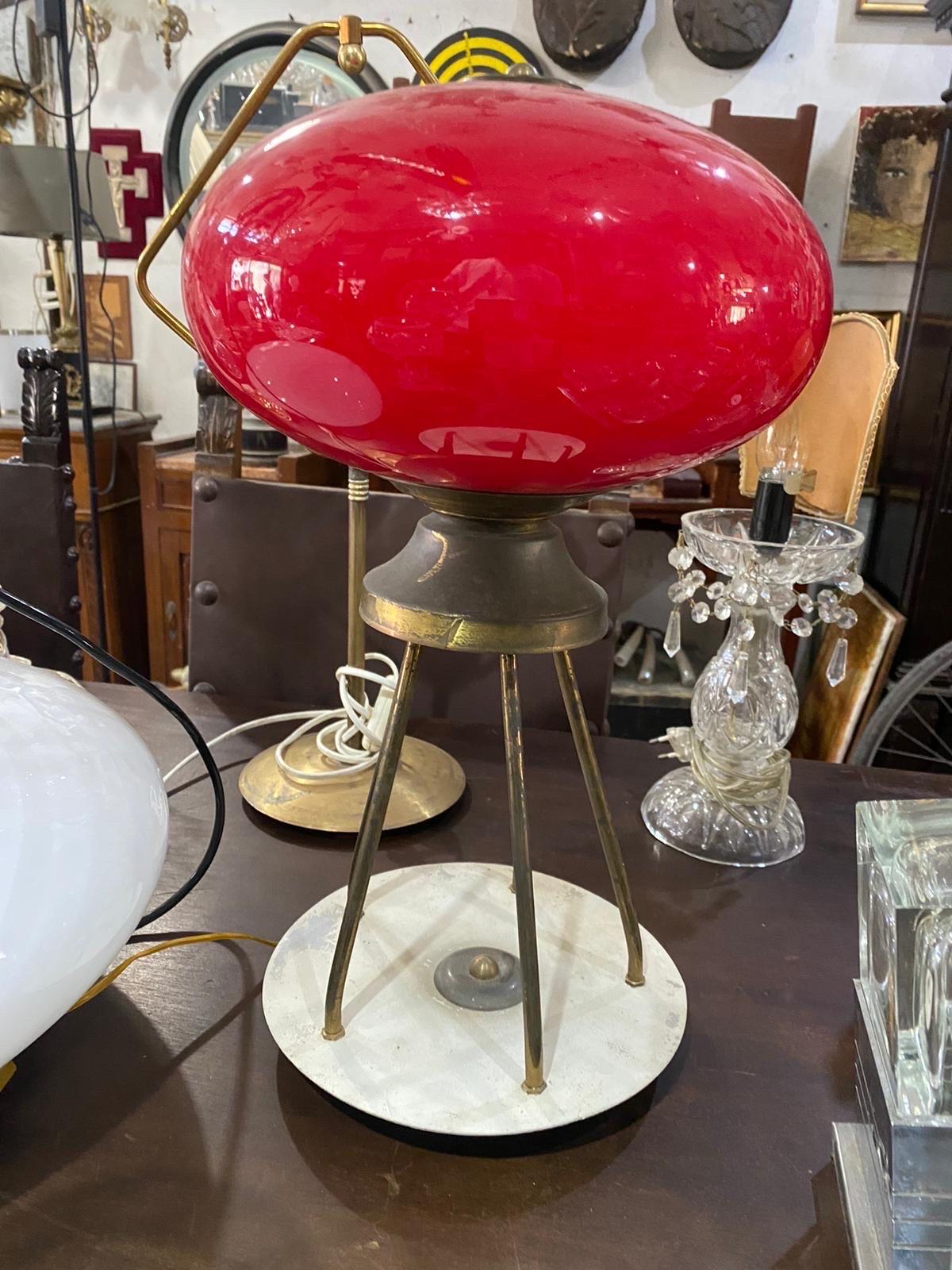 Esta lámpara de sobremesa moderna de mediados de siglo, diseñada y fabricada en Italia en los años cincuenta a la manera de Giuseppe Ostuni, presenta una llamativa pantalla de cristal rojo con una forma suave y redondeada que le da un aspecto