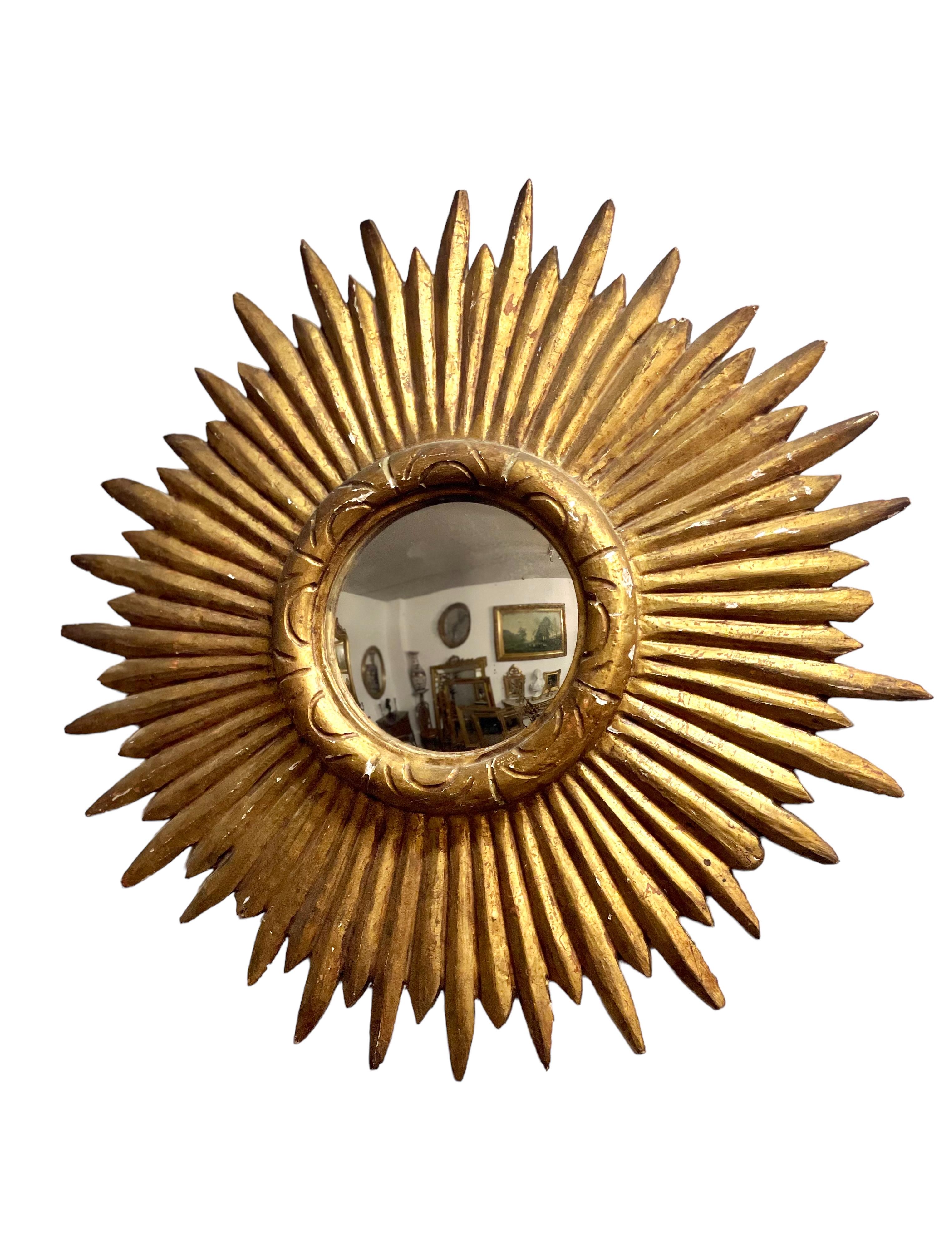 A fabulous midcentury sunburst mirror, with the original gilt finish on the finely carved wooden feathered rays, and a circular, light diffusing convex mirror within. A truly stunning piece, this would add a delightfully stylish gleaming accent to
