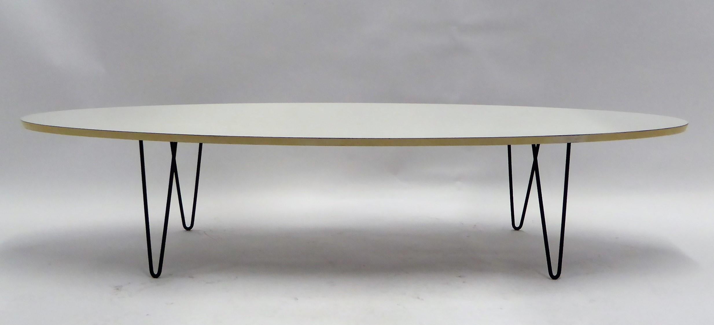 Midcentury classic look with this period Surfboard coffee cocktail table on hairpin Legs. With a elliptical white formica top, white lacquered edge, raised up on four black wrought iron hairpin legs. In very, very good condition with minor flakes