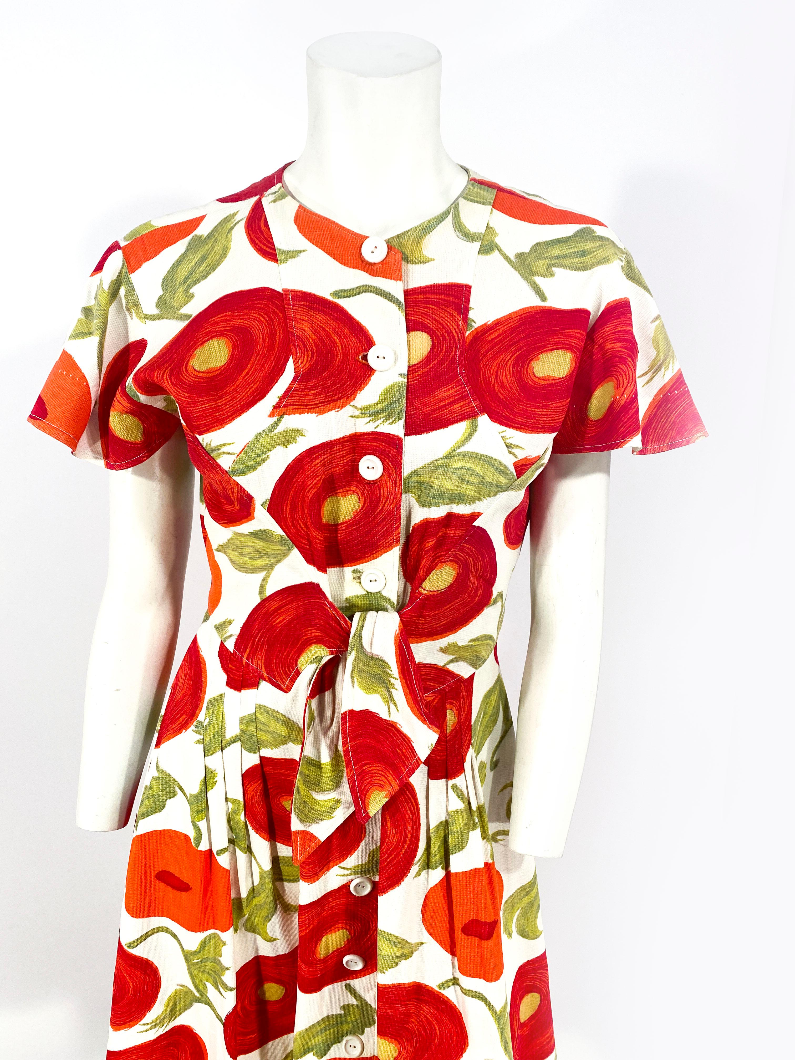 1950s surreal floral printed day dress made of a cotton pique. The structure of the dress features an enlarged caplet sleeve, incorporated tie-sash in the front, button opening along the face, and a pleated skirt.