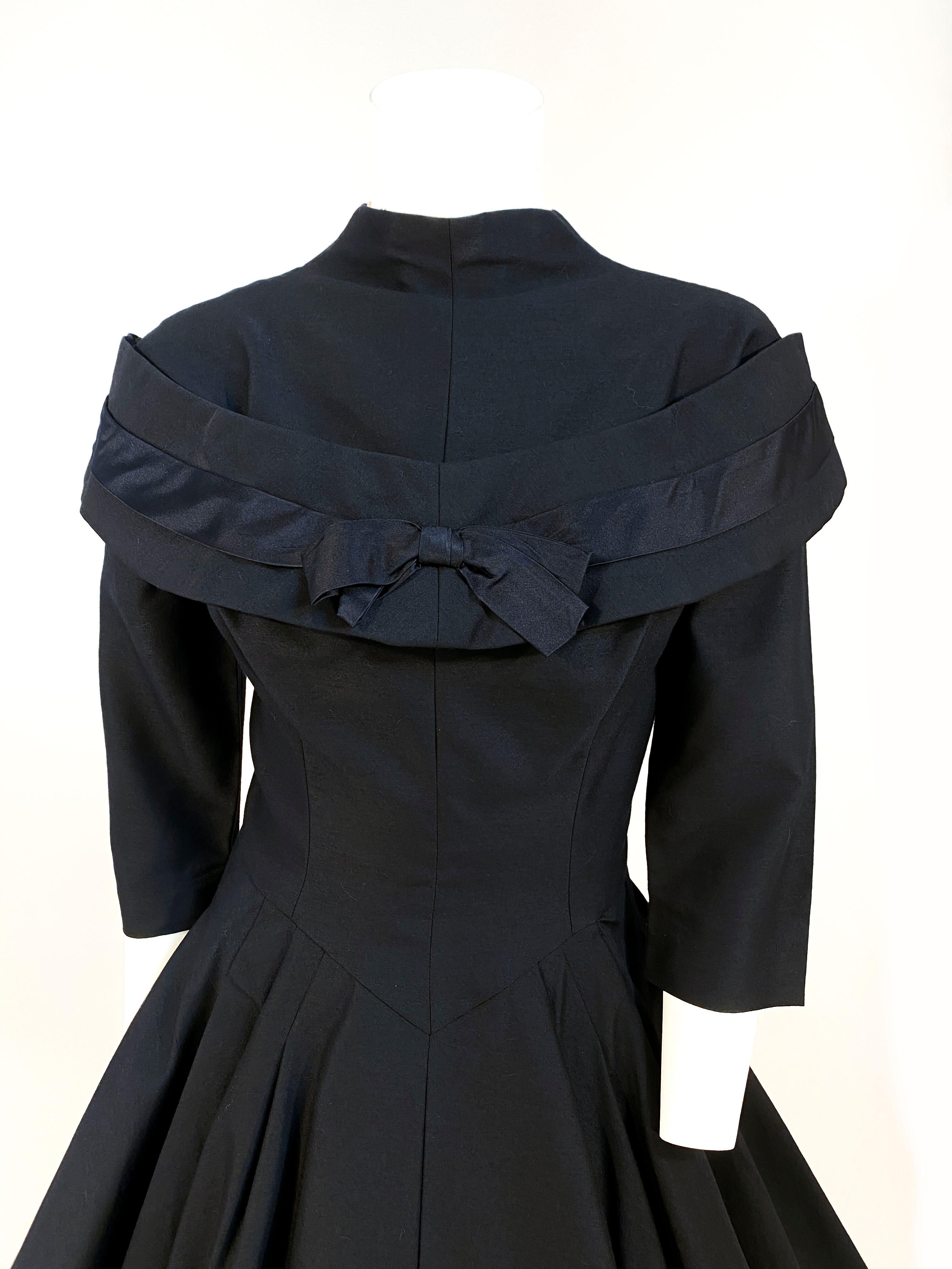 1950s Suzy Perette black wool cocktail dress with a full circle skirt backed in peplum for extra structure. The sleeves are three-quarter length, the neckline is high with a decorative secondary collar done in layers of wool and satin, finished with