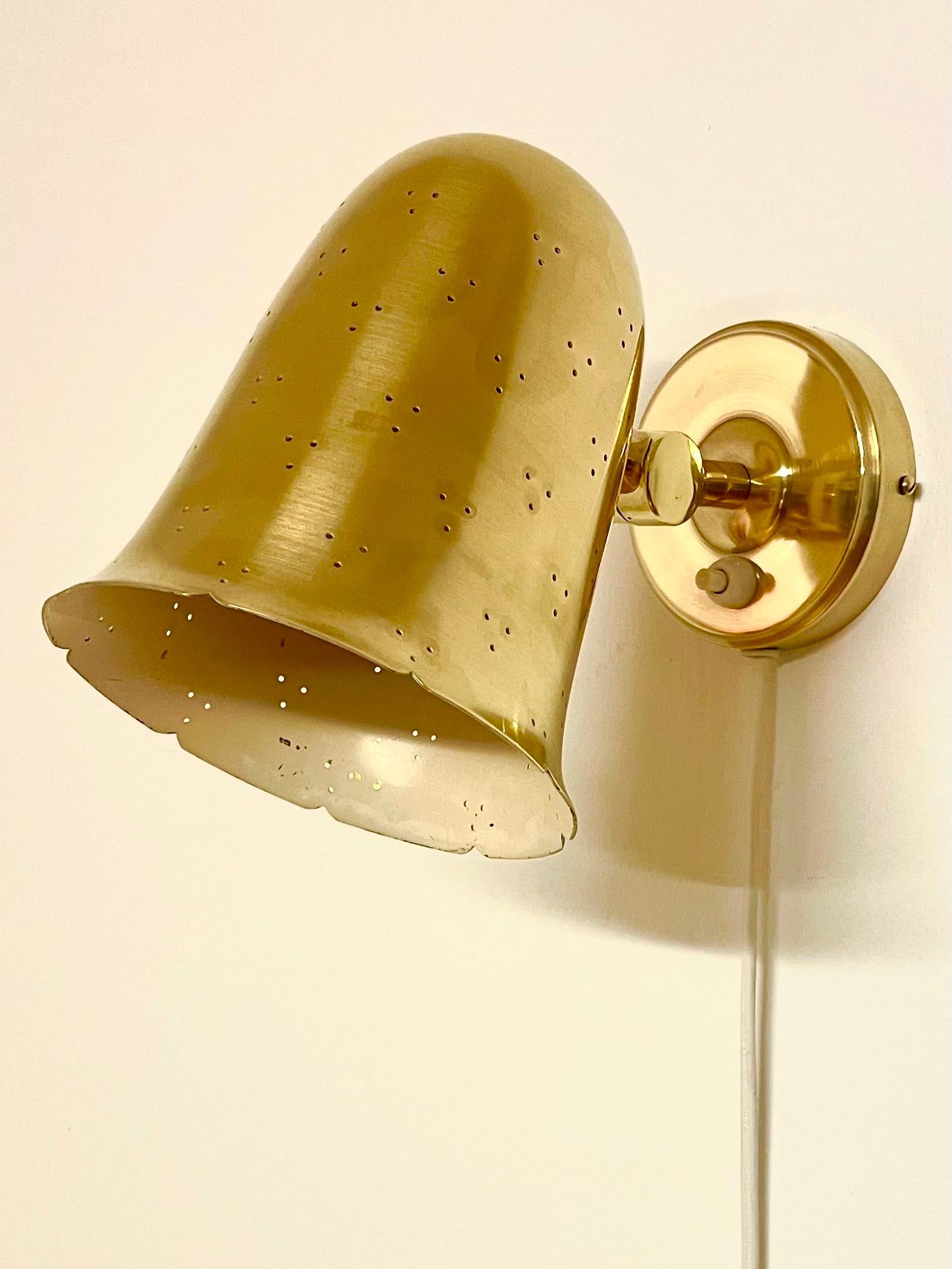 This is the Swedish 1950s wall lamp no. 6501 manufactured by Boréns in Tranås. 
It comes made in brass with a bell-shaped shade with perforated pattern. The surface is shiny and bright. 

The circular wall mount is connected to the shade by a