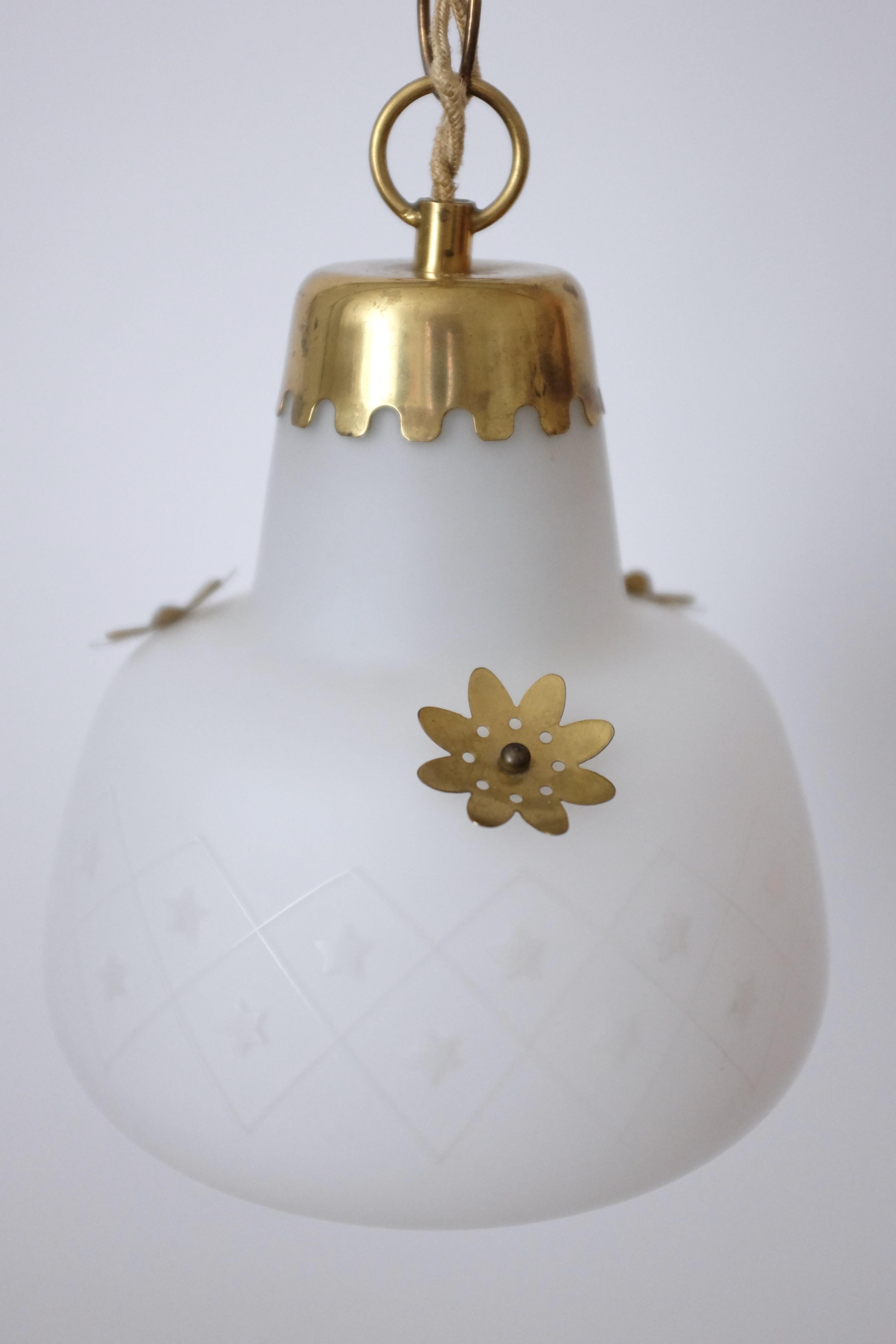 Charmant pendentif Vintage des années 1950 en laiton et verre opalin provenant de Suède. Verre gravé de couleur laiteuse avec des détails décoratifs en laiton de forme organique. Le verre présente des détails ondulés autour du fond de la lanterne