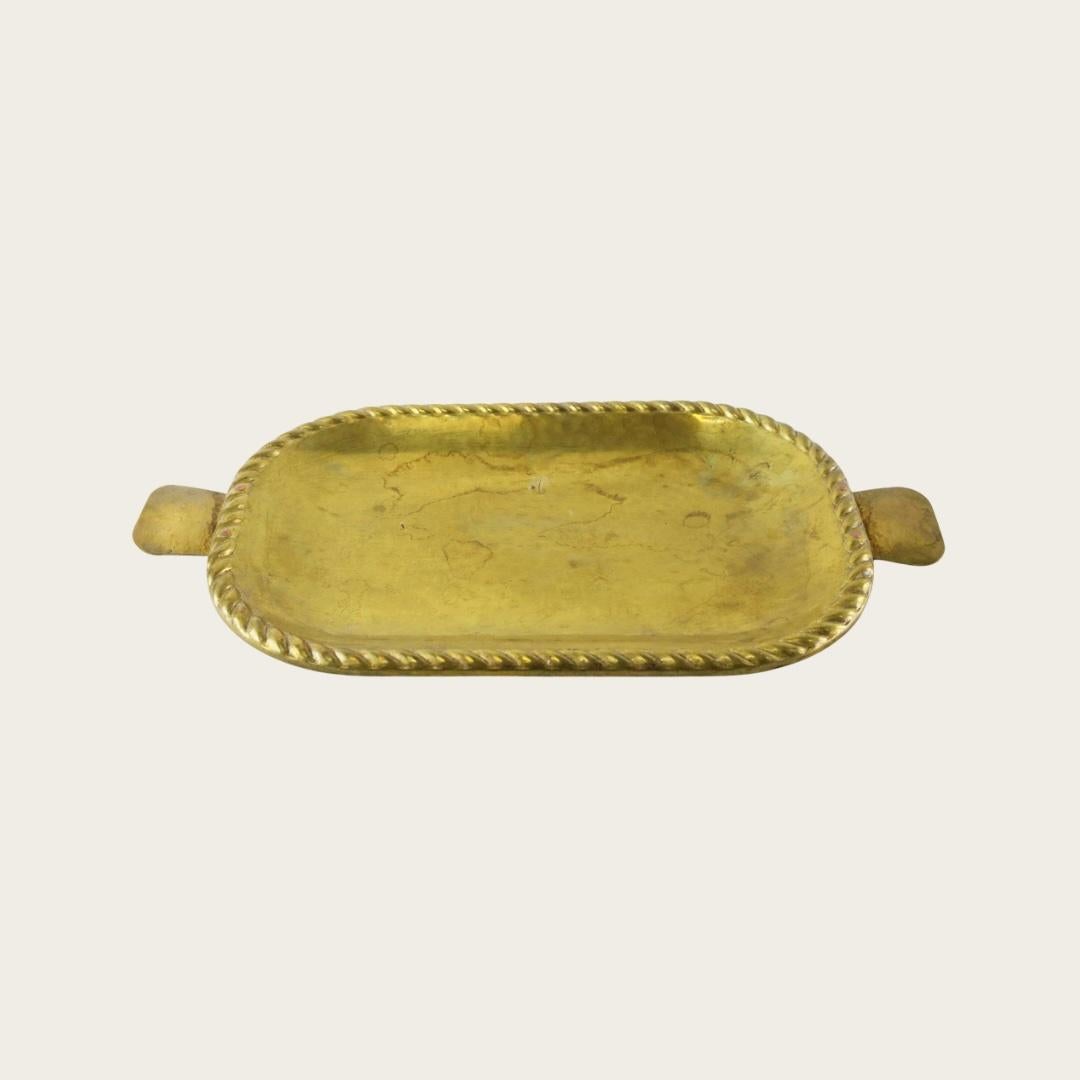 Años 50, Suecia. Con un elegante diseño de cuerda trenzada grabado en su superficie y graciosas asas curvadas. Esta bandeja sueca vintage de latón aporta el encanto de mediados de siglo a cualquier espacio. Dos disponibles. Se venden por unidades.