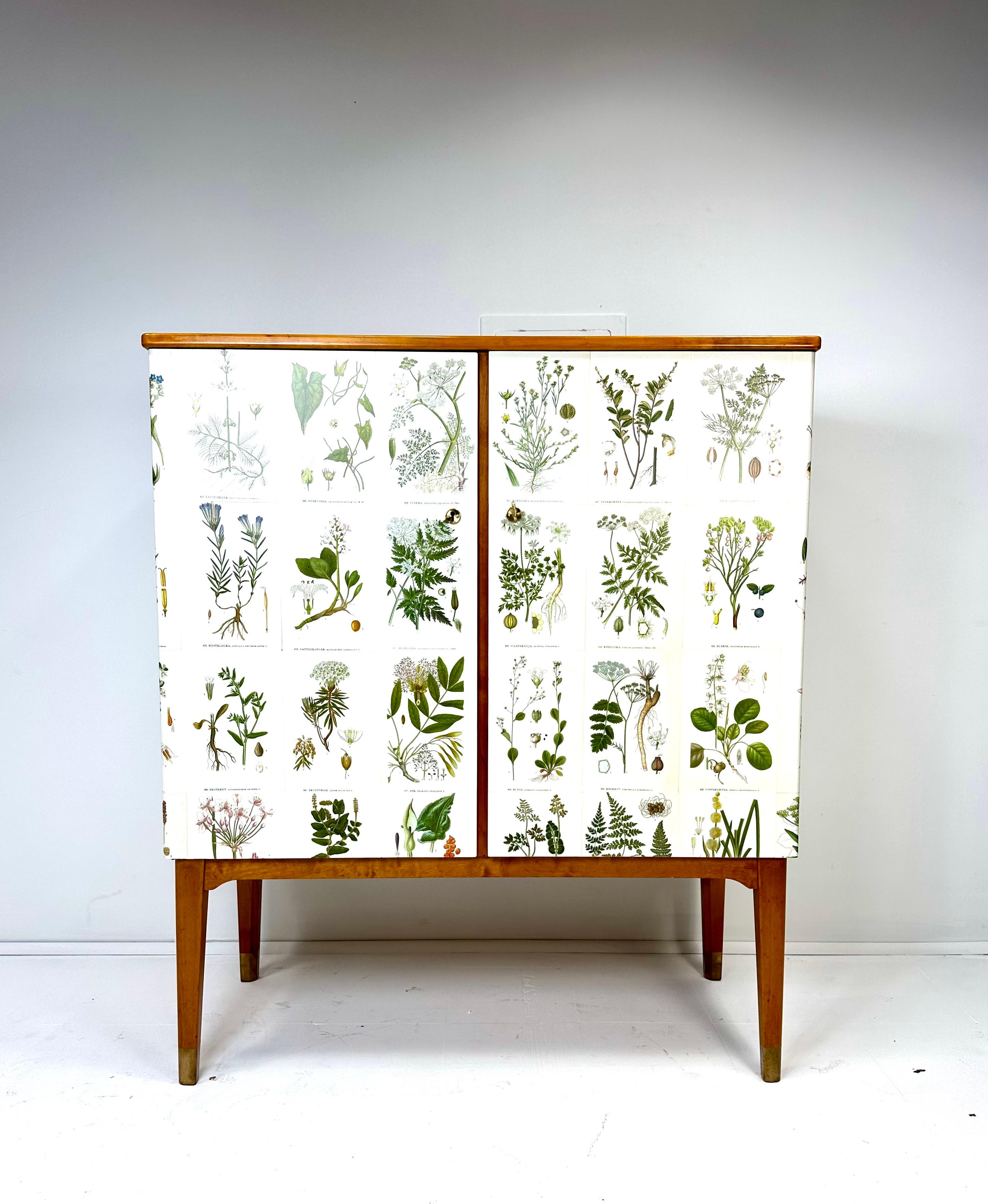 1950’s Swedish Cabinet later papered with illustrations by C.A. Lindman book Nordens Flora.

Cabinet consists of 2 large doors concealing adjustable interior shelves on the right side and open drawers on the left side. Brass tipped legs.

Key