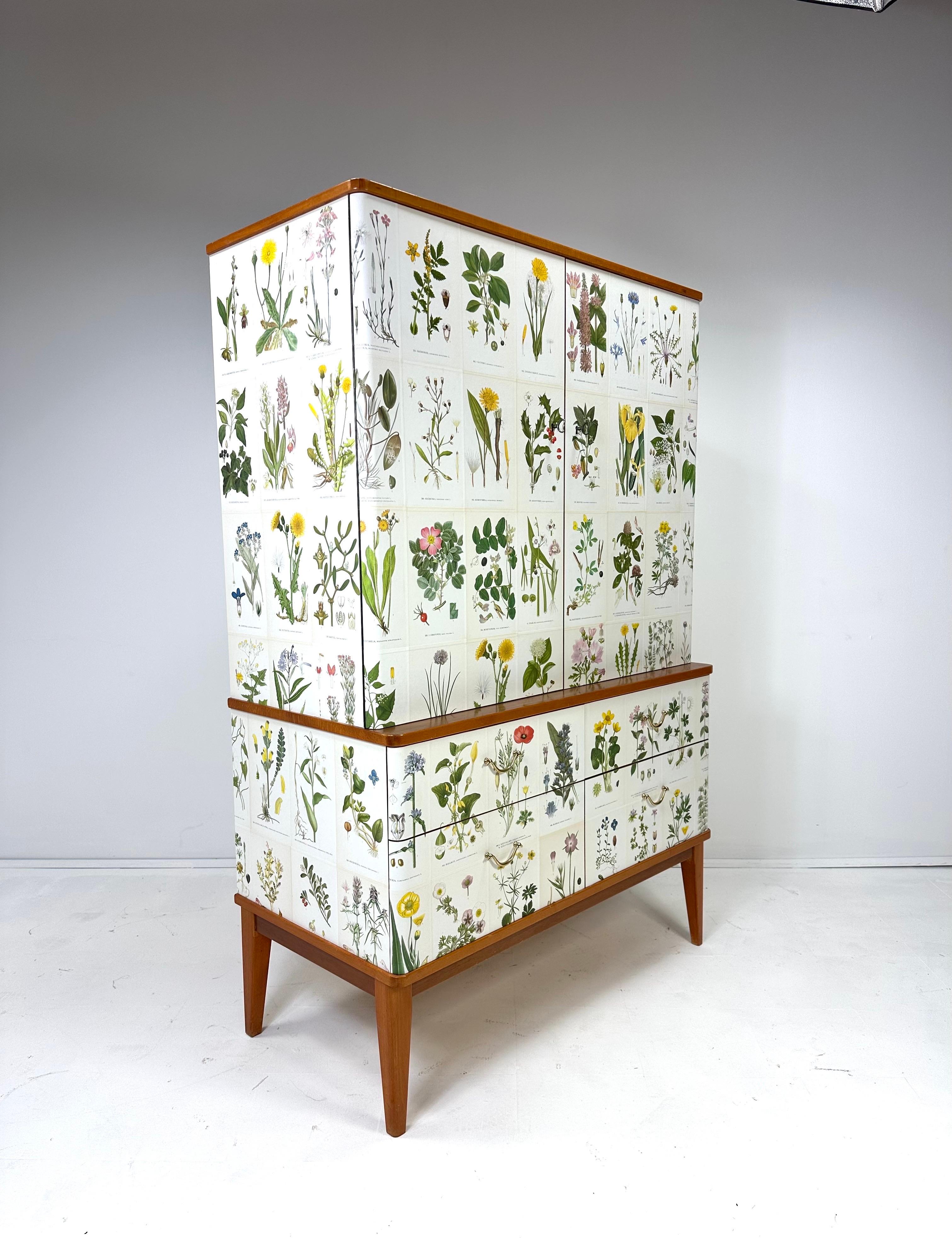 1950’s tall Swedish Cabinet later papered with illustrations by C.A. Lindman book Nordens Flora.

Cabinet consists on top of 2 large doors concealing adjustable interior  shelves and 2 small drawers.  The bottom of the cabinet consists of 4
