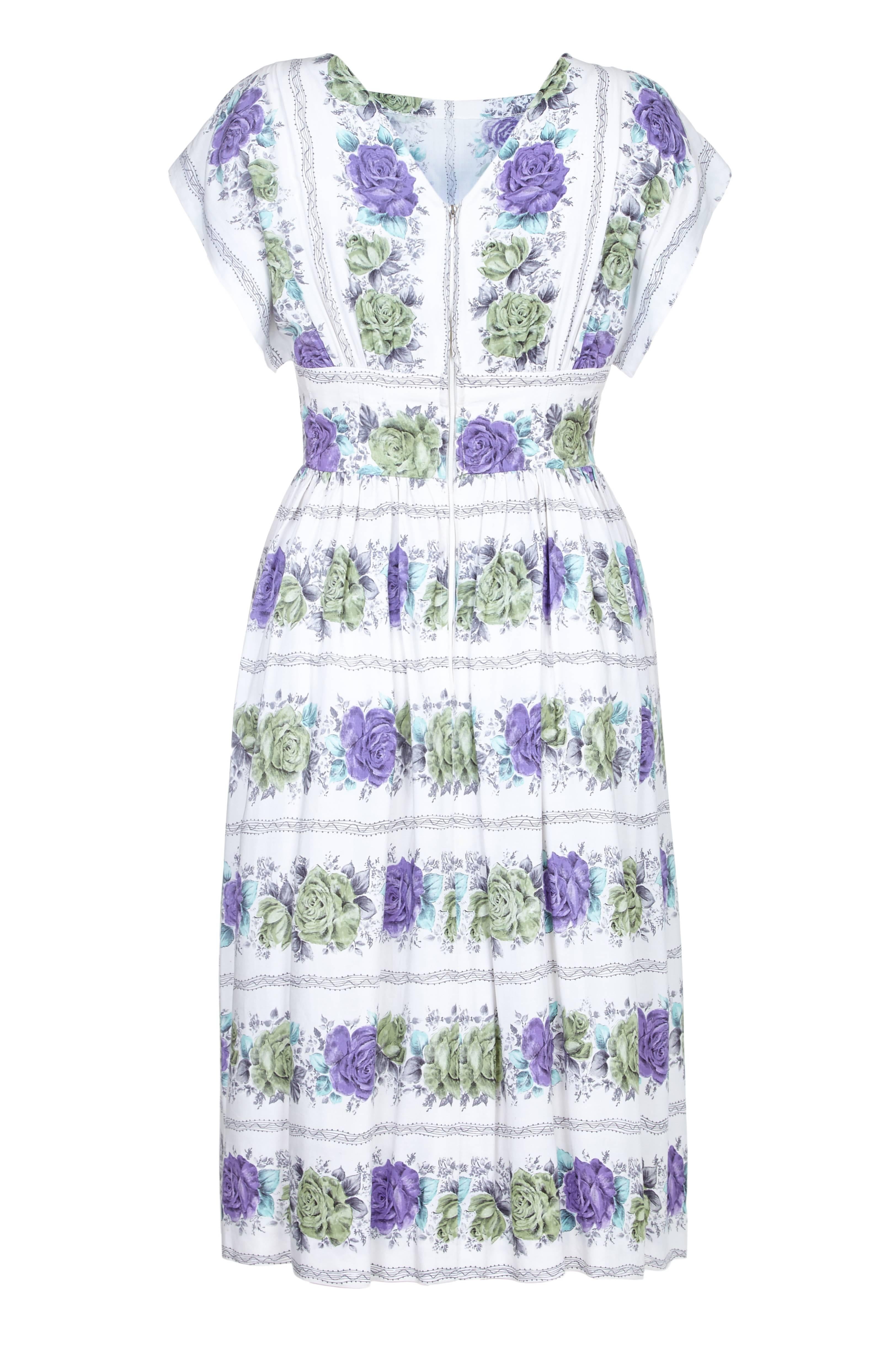 This lovely 1950s white cotton rose print dress is skilfully made and in pristine vintage condition. The fine printed cotton is soft to touch and of notable quality, featuring a pretty linear rose design in pale green, violet and turquoise which