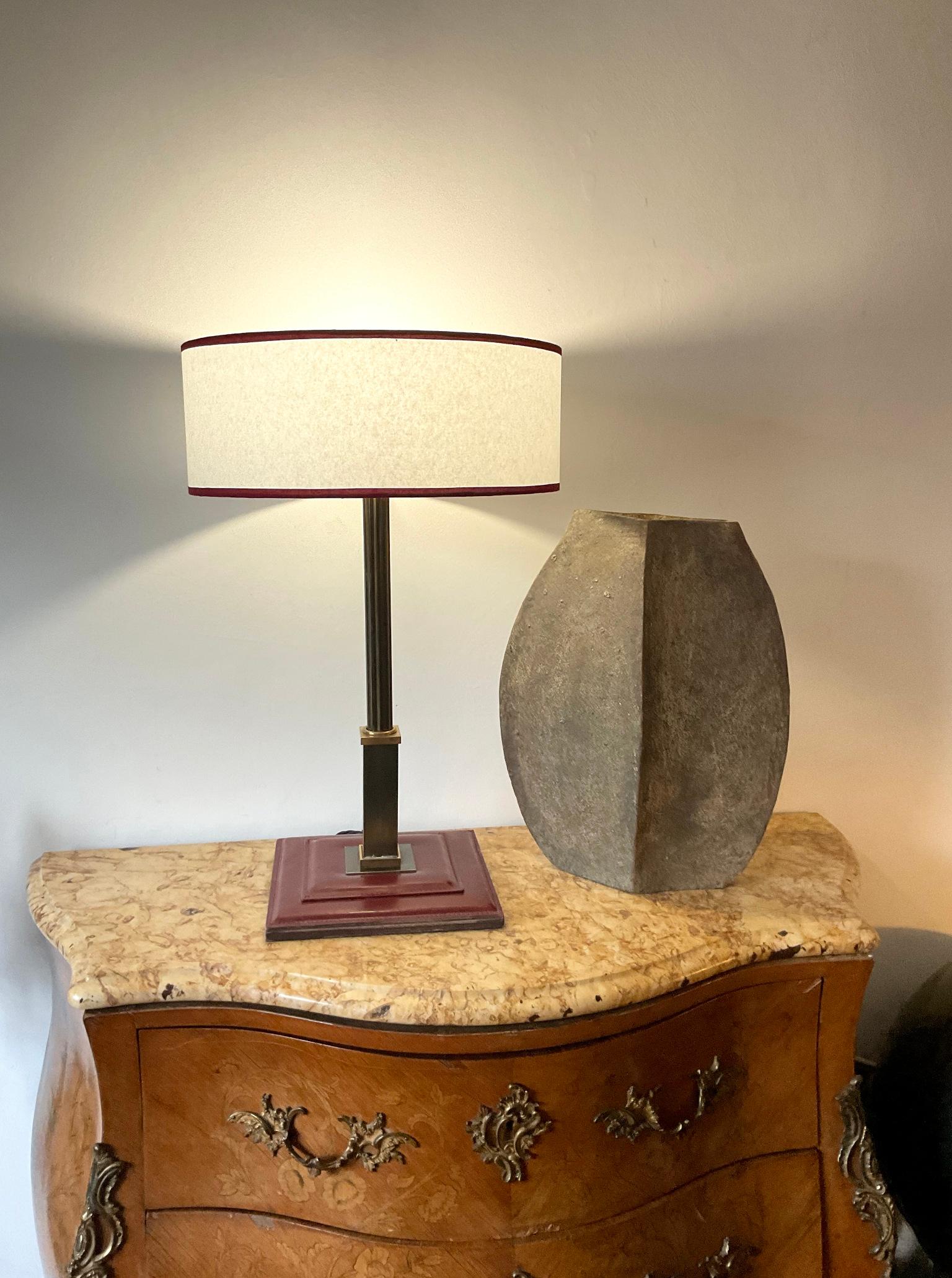 Neoclassical table lamp from the 1950s in the style of Maison Longchamp or Maison Hermès.
Brass body with full-grain leather base and burgundy saddle stitching.
Topped with a parchment shade with burgundy fabric binding.
