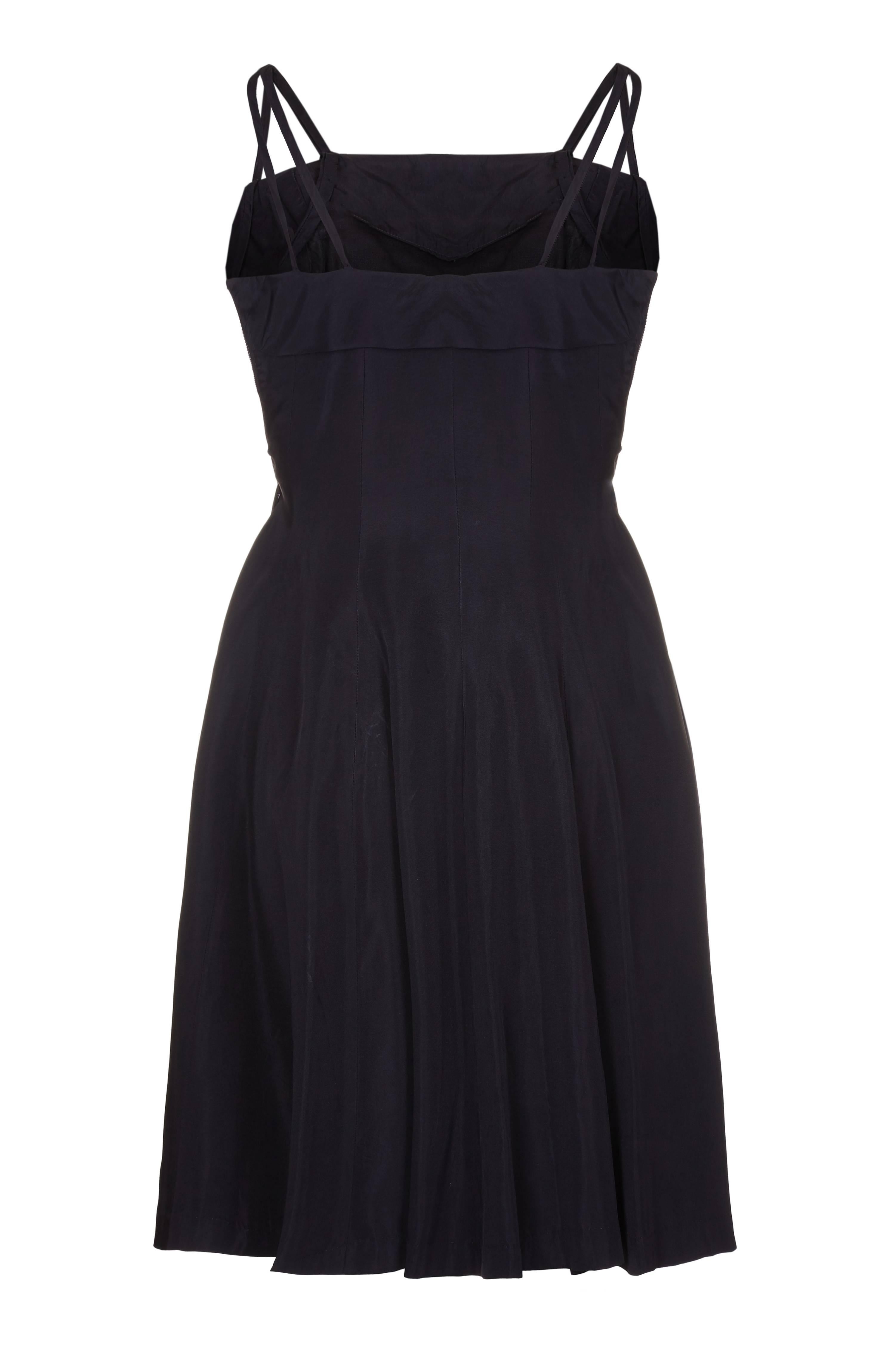 Cette charmante robe de soirée des années 1950 en taffetas noir brodé avec des bretelles croisées est gamine, féminine et en très bon état vintage. Les exquises fleurs brodées commencent au niveau du buste et tombent doucement sur les hanches, ce