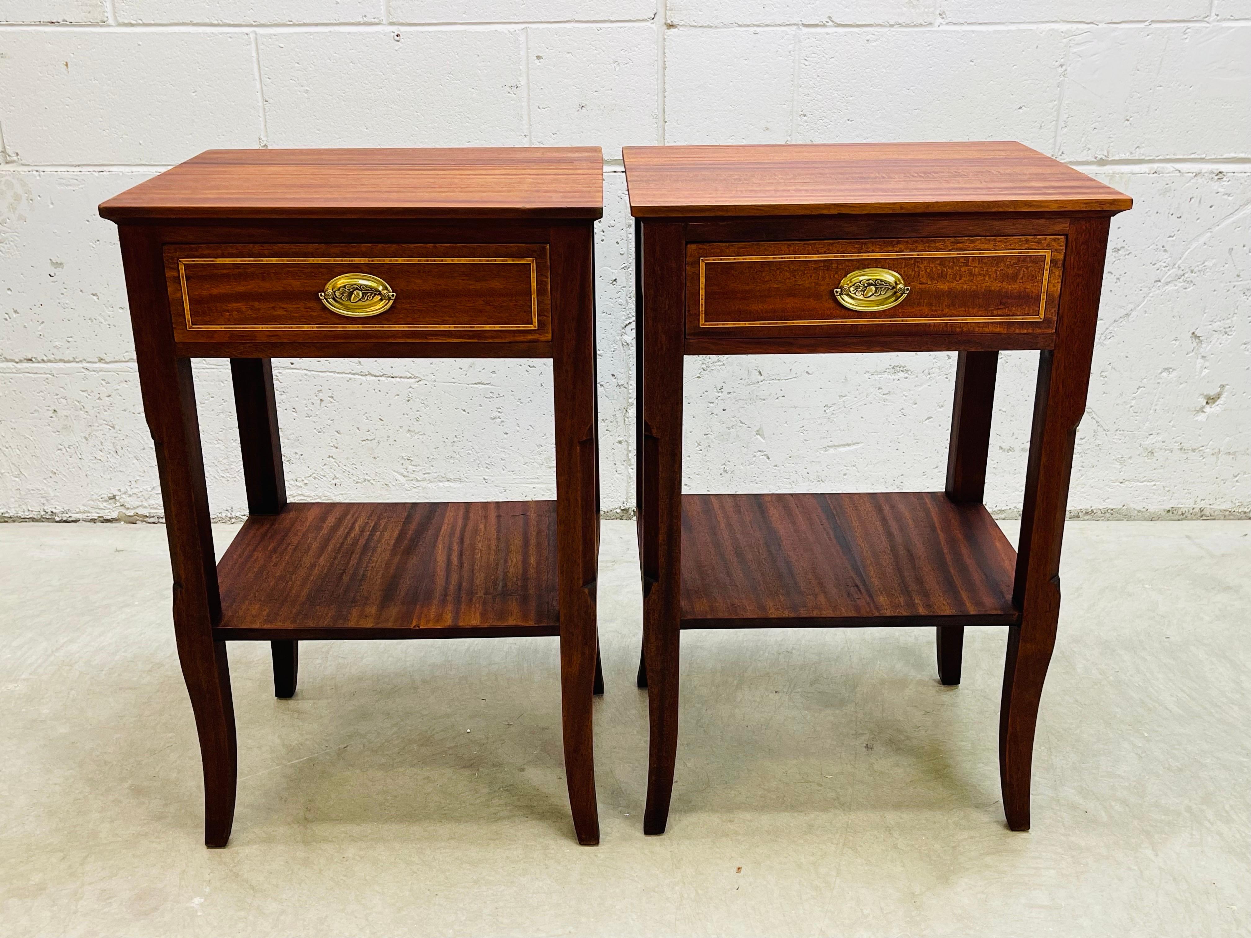 Vintage 1950s pair of tall mahogany nightstands. The nightstands have a single drawer and a shelf for storage. The brass pulls have an acorn design. Each drawer has an inlaid pattern. The shelf is 11”H. Excellent refinished condition. No marks.