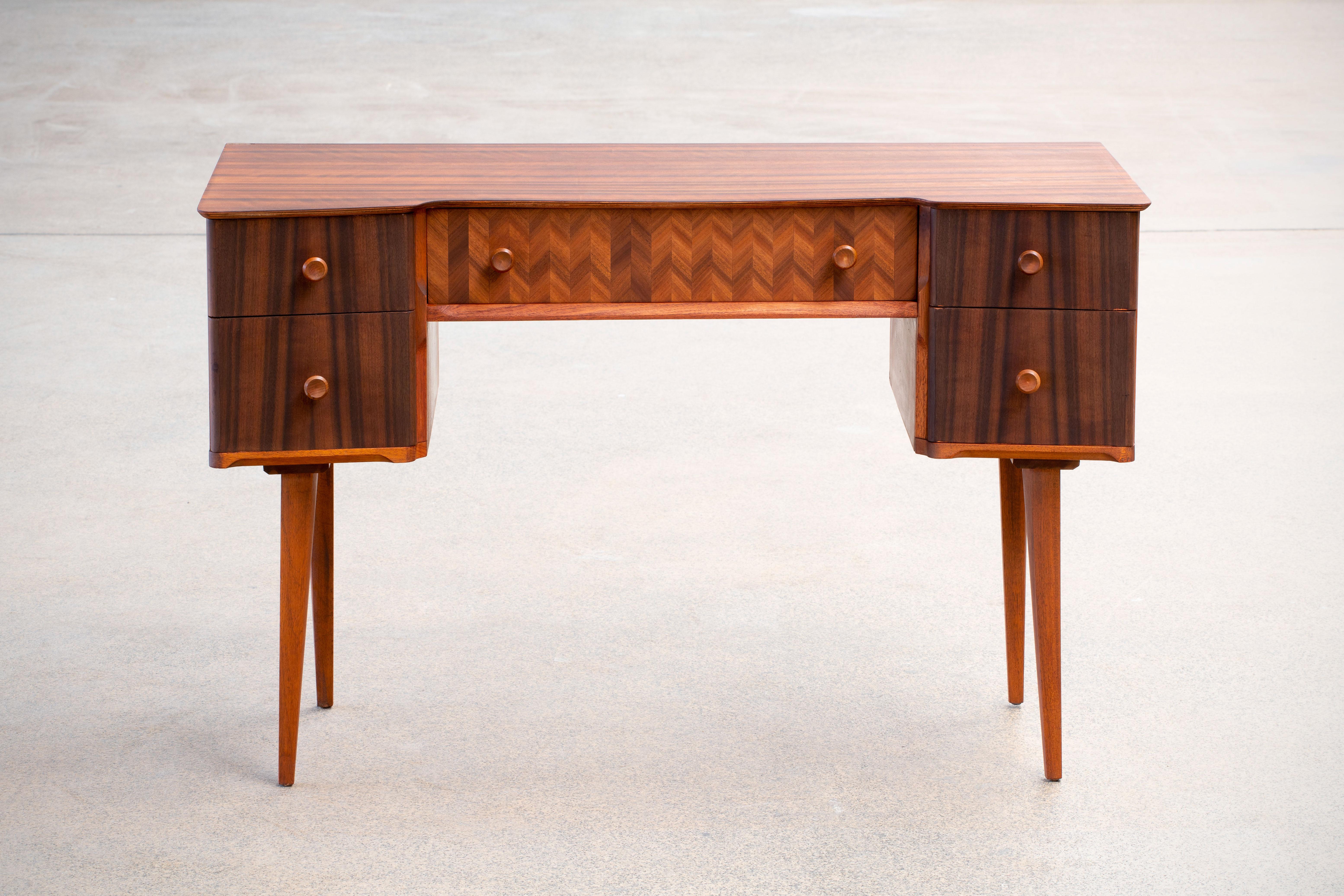 Beautifully designed writing desk in teak and walnut. With a very distinct design this desks every wood surface has been given specific angles such as the tabletop, the unit with drawers as well as the legs. The desk is given a very light and airy