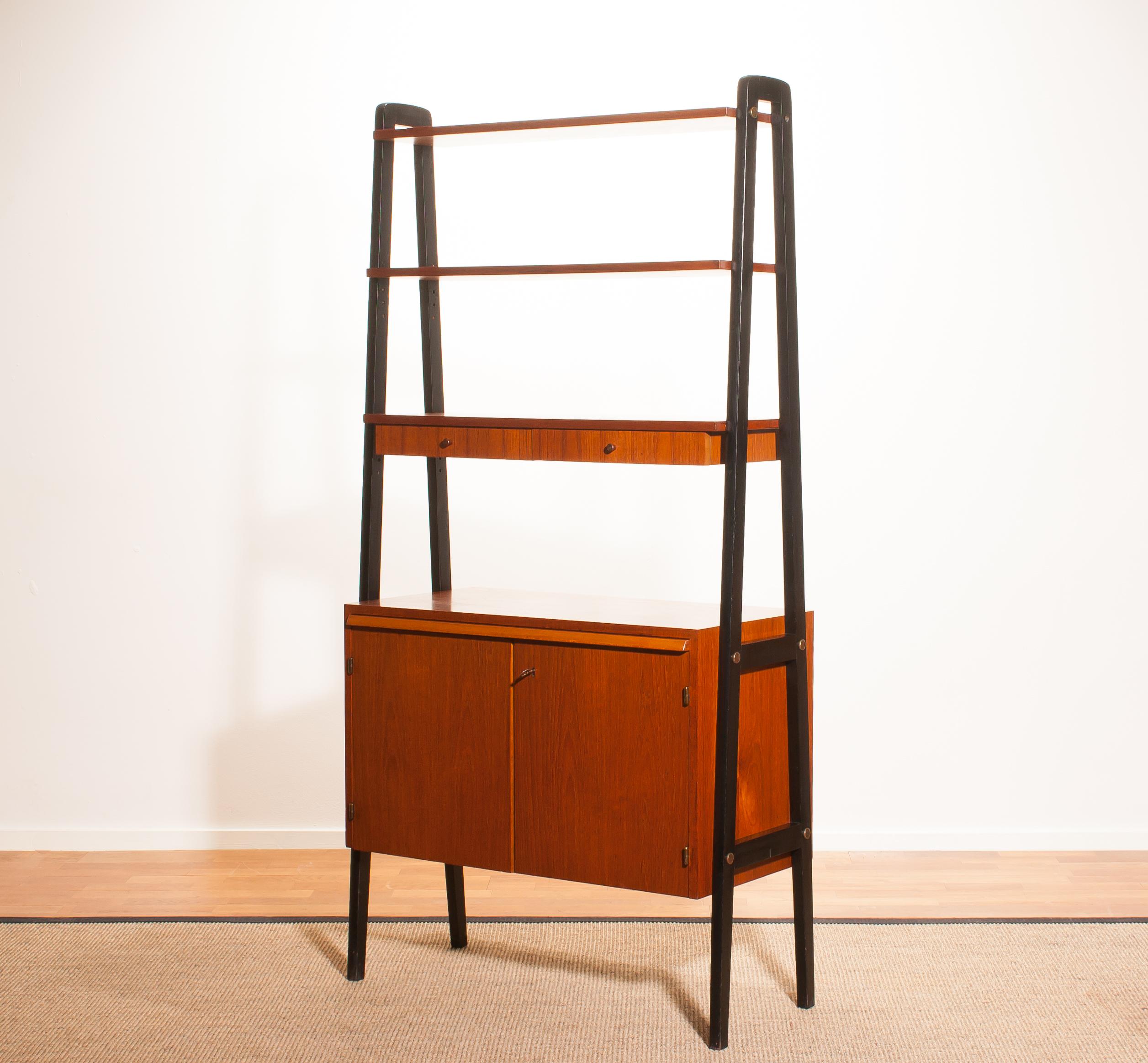 Beautiful cabinet, room divider, bookcase, secretaire in teak with black stands.
This cabinet has got two shelves, one shelve with two drawers, two doors and a slidable writing space.
It is in a very beautiful condition.
Period 1950s
Dimensions