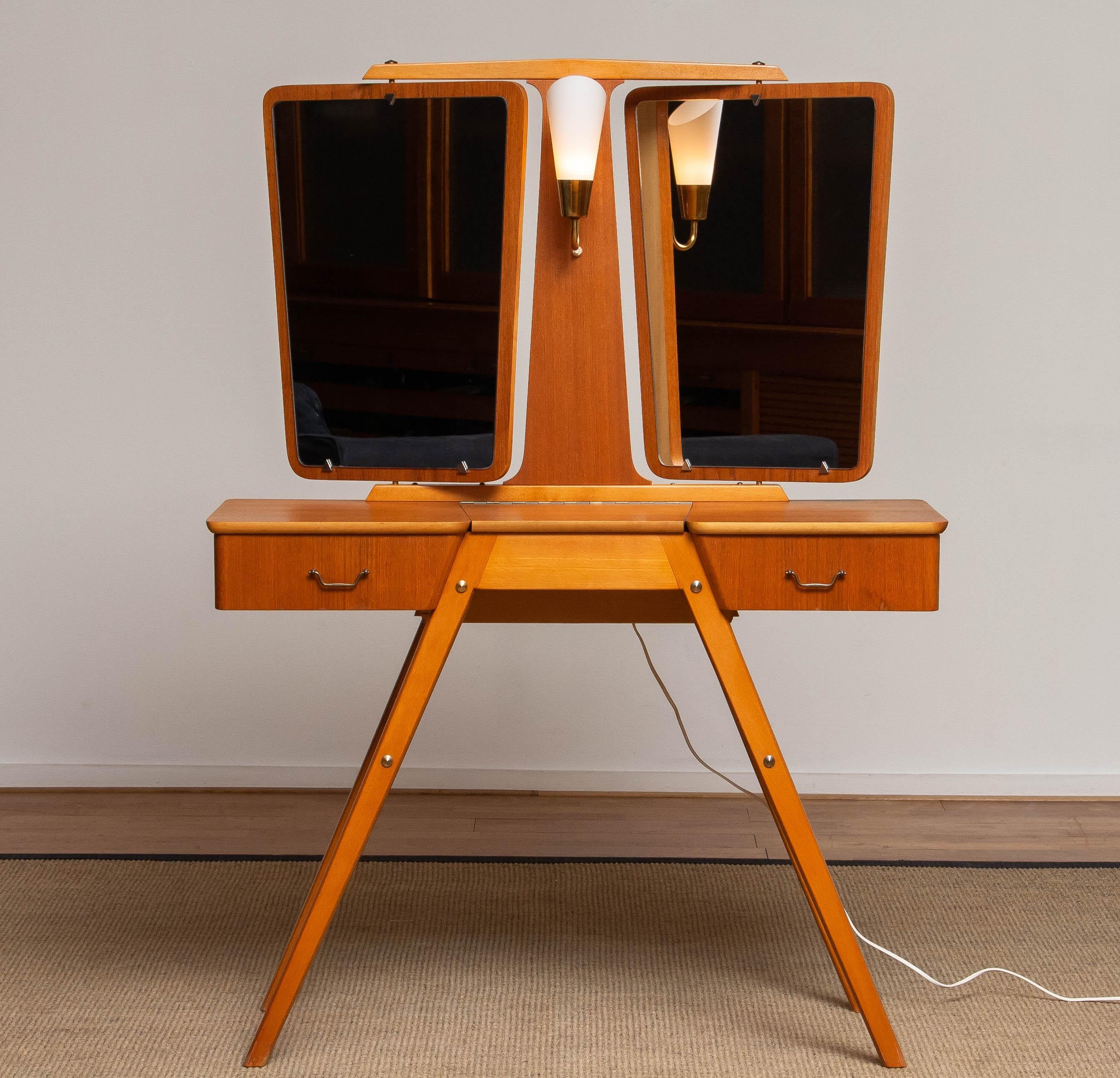 Absolutely beautiful vanity dressing table made by G&T Sweden in the 1950's. 
This vanity has two mirrors who can revolve and a central light who can be switched in the front between the two mirrors.
Two shelfs in the front and a opening door on