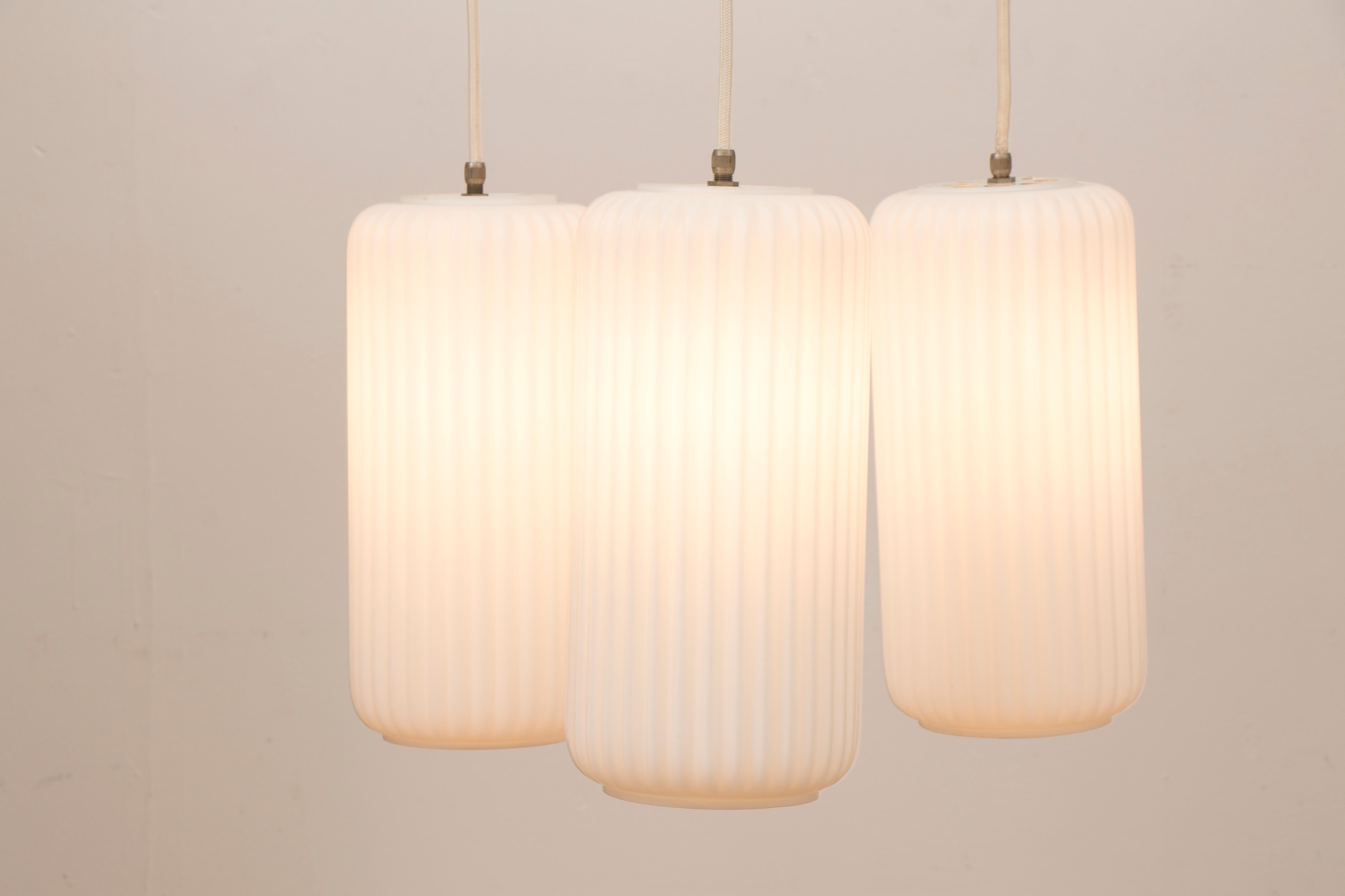 A 1950s 3-shade cascading Italian opaline glass hanging pendant light. Each of the large Minimalist, opaline, ribbed glass, shades hang from a white metal three-pronged ceiling fixture which are adjustable in height to meet your requirements. A