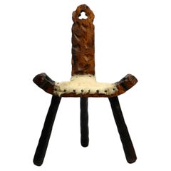 Antique 1950s three-legged stool made of solid wood in black-brown with cowhide seat