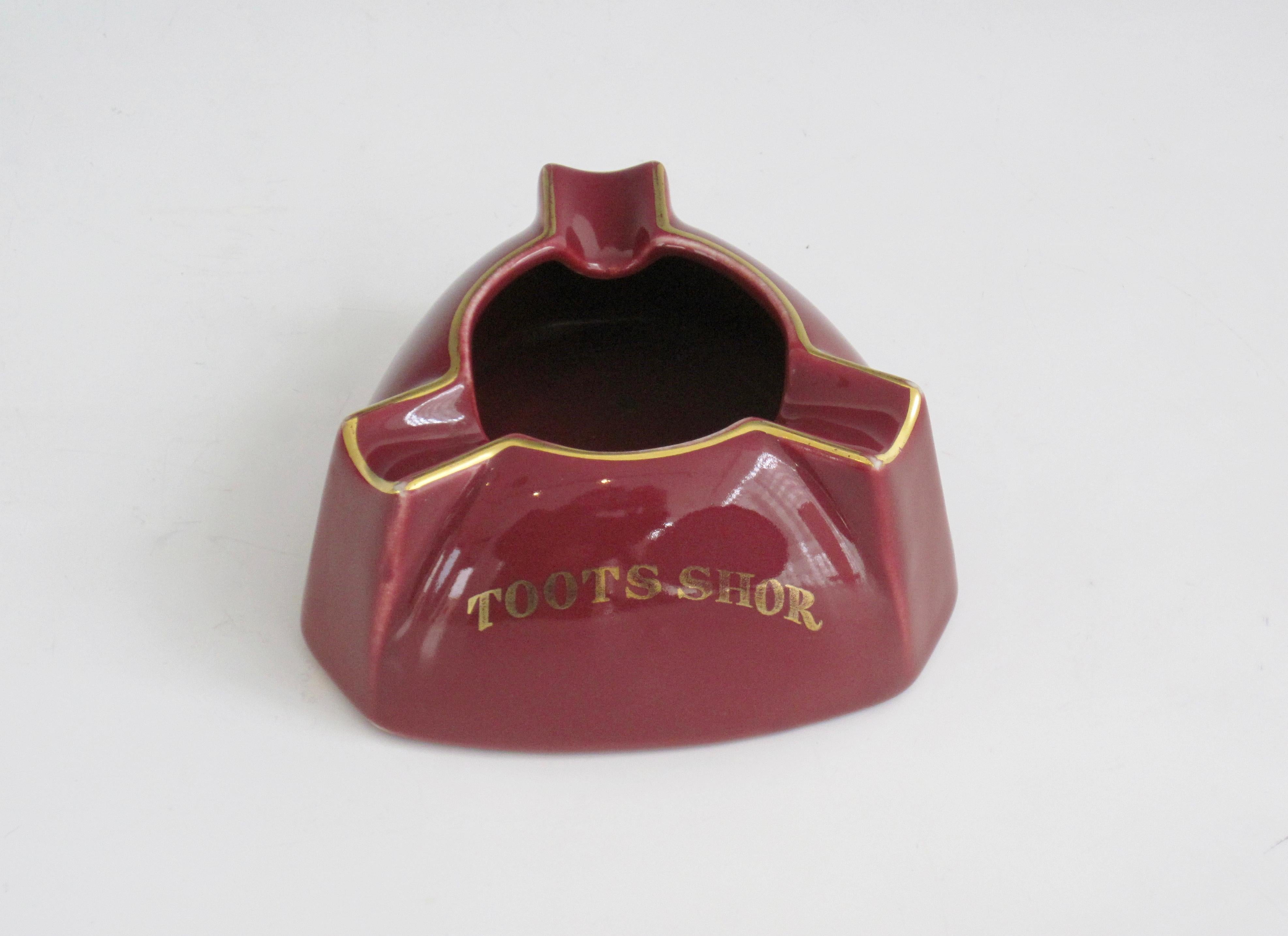 A triangular shaped maroon or burgundy and gold TOOTS SHOR ashtray from the legendary Toots Shor restaurant and lounge in NYC. c.1950 Hallmark on underside.
Toots Shor's Restaurant was a restaurant and lounge owned and operated by Bernard 