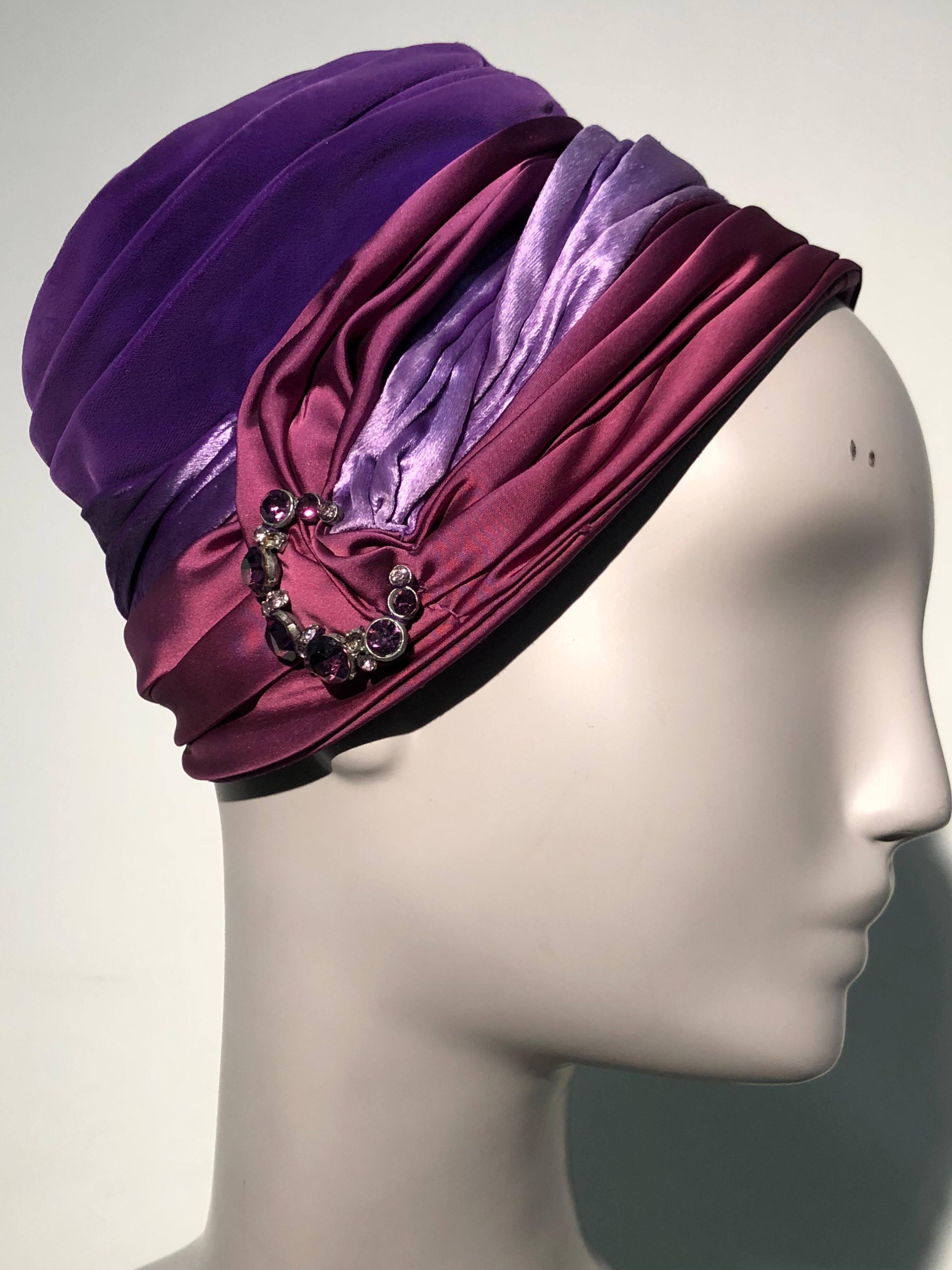 A gorgeous 1950s turban-styled hat in purple velvet, purple satin and burgundy satin with a rhinestone and pearl brooch at front. No maker label present. 