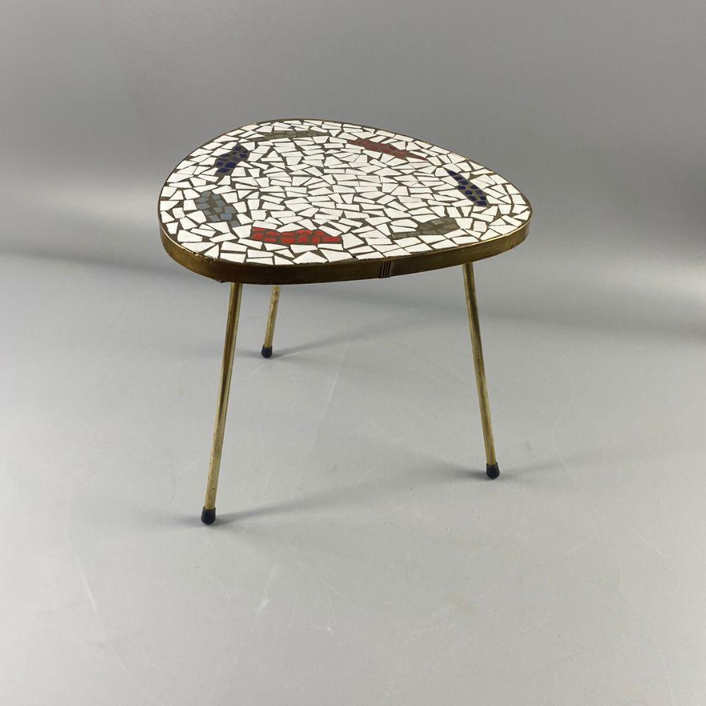 This small mosaic table made around 1950-60. It stands on three copper legs, and the edges of the table are closed with copper inlays. On the top is a mixed white and colored mosaic. Due to its age, the patina of the copper is visible in some