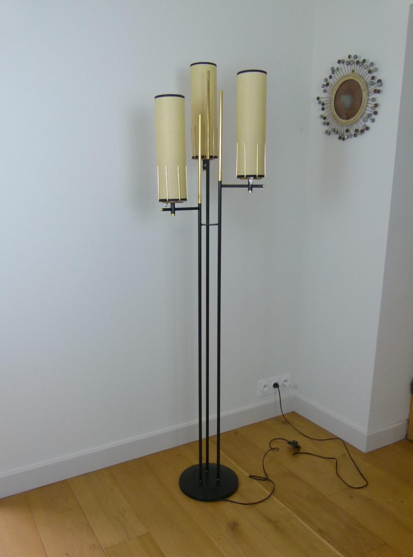 Floor lamp with three-light composed of a circular base in black lacquered metal, on which are fixed three-light arms in black lacquered metal, surmounted by tubular shades in ivory-colored parchment.
Brass rods arranged around the light covers