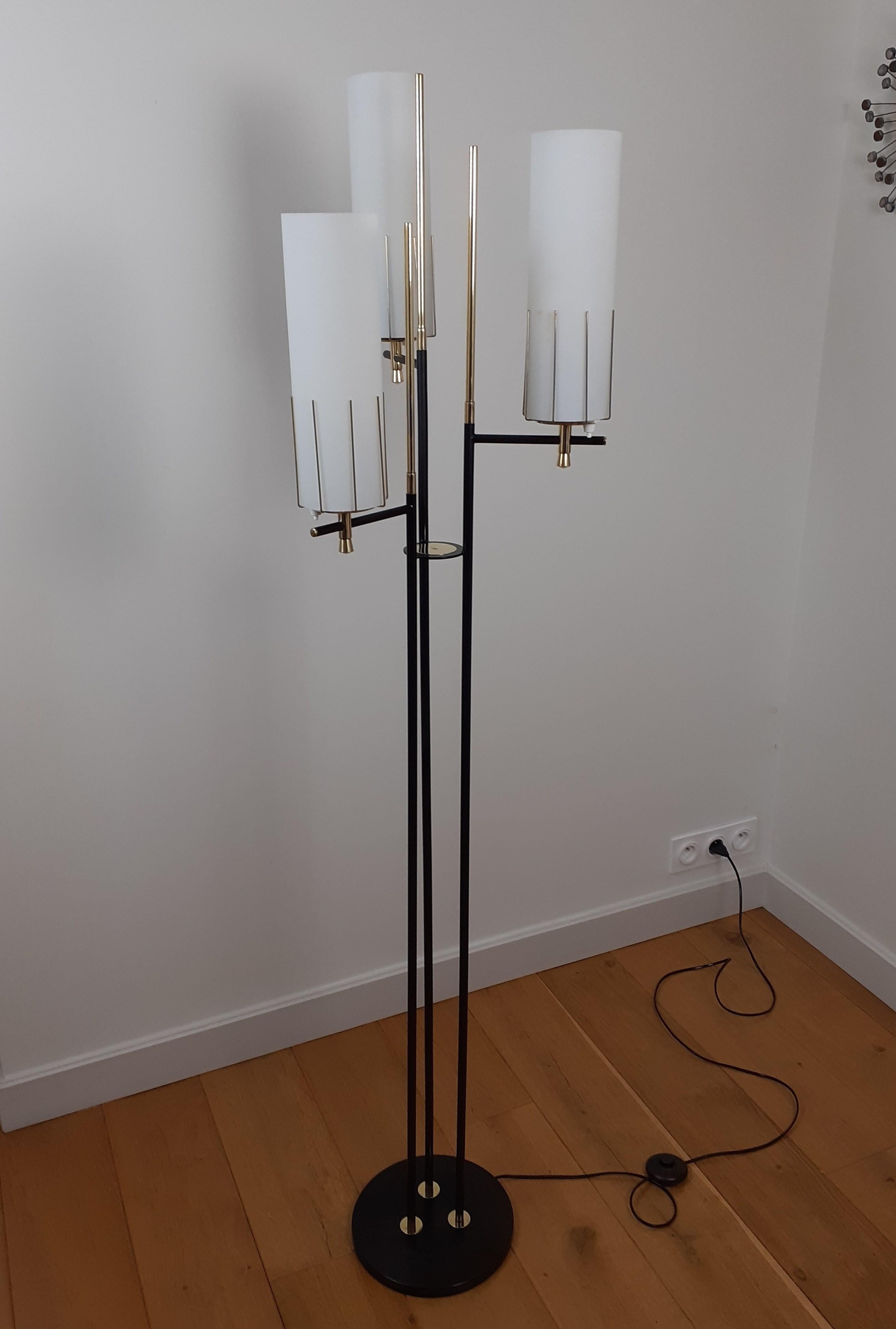 Floor lamp with three lights composed of a circular base in black lacquered metal, on which are fixed arms with three lights in black lacquered metal, surmounted by tubular lampshades in opaline glass.
Brass rods arranged around the lamp covers