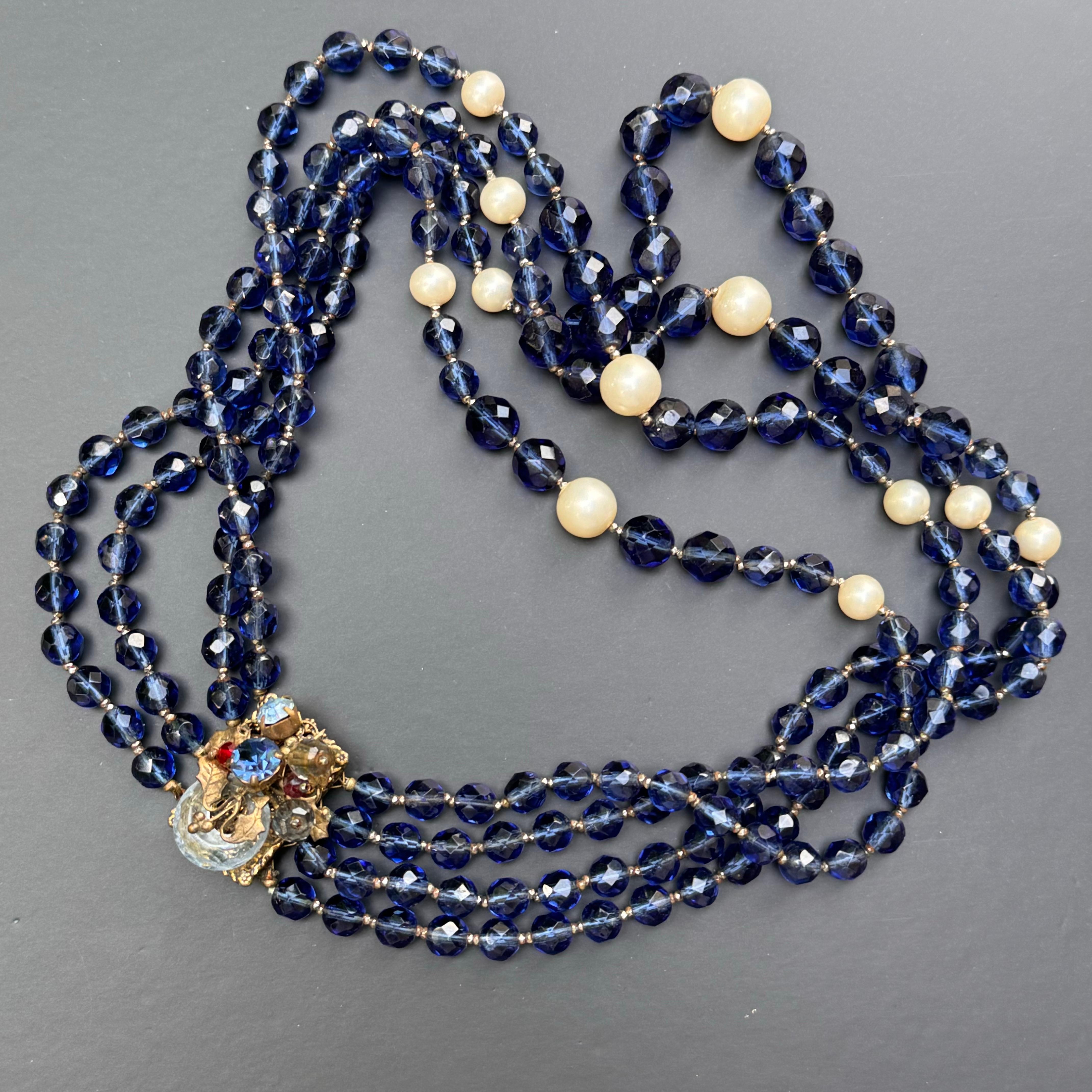 Aggiungi un tocco di glamour vintage anni '50 alla tua collezione di gioielli con questa squisita collana a strati. Con perle di cristallo sfaccettate in un'ipnotica tonalità di blu, questo pezzo emana eleganza e raffinatezza. Il design è