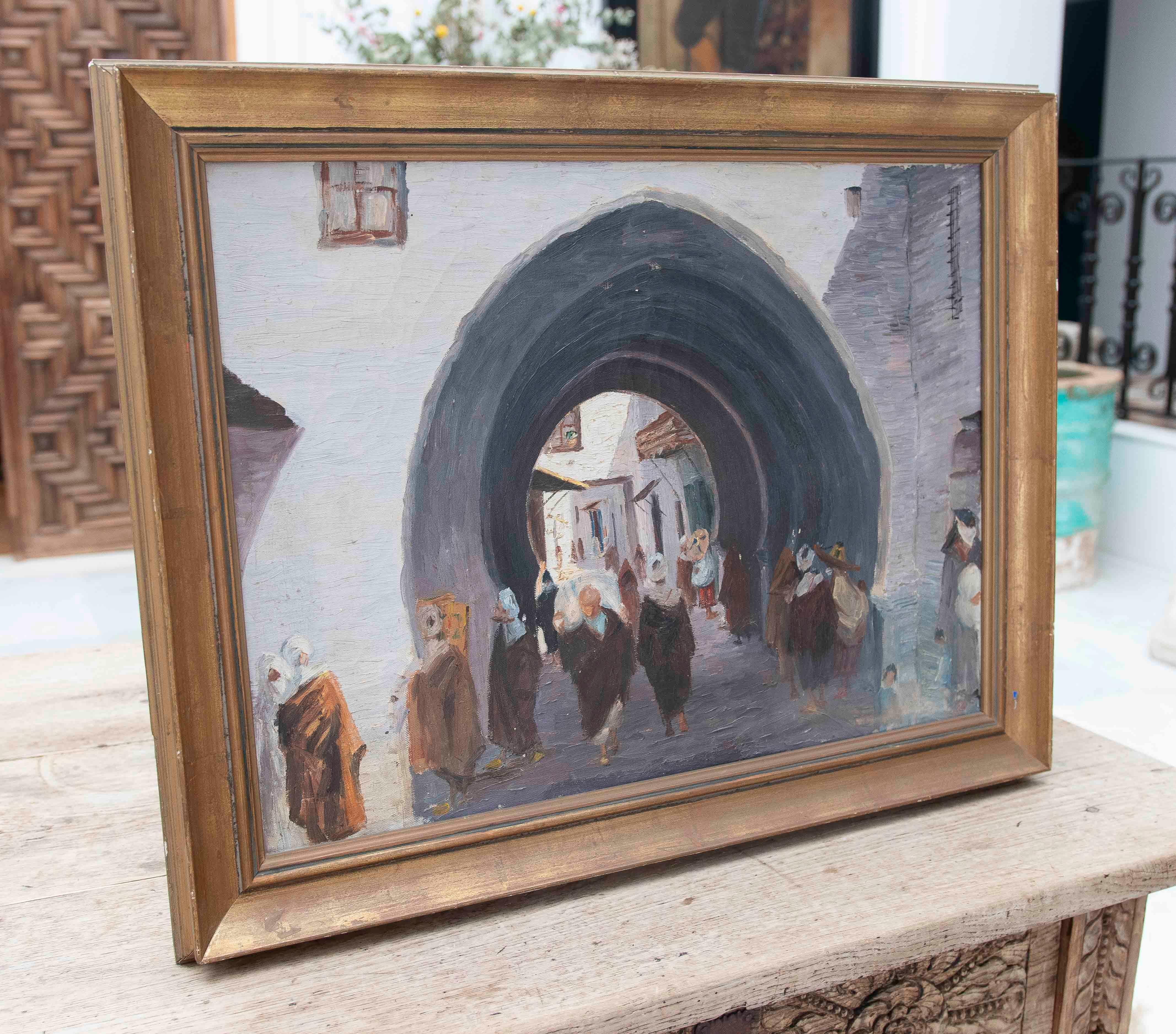 Oil painting depicting an urban passageway covered by an imposing architectural arch, characteristic of North African medinas. The composition features multiple figures dressed in traditional robes, some interacting and others moving along the