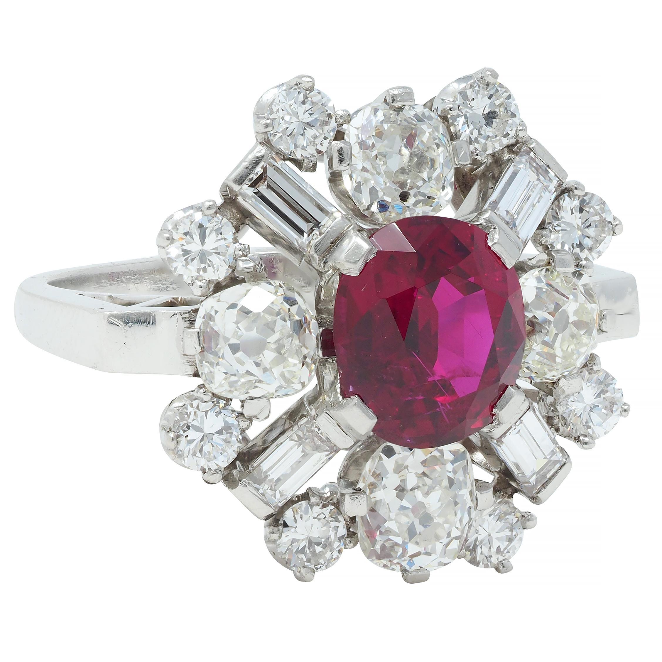 Centering an oval cut ruby weighing 2.17 carats - transparent medium purplish red in color 
Natural Thai in origin - set with tab-like prongs with a clustered burst motif halo
Comprised of old mine, transitional, and baguette cut diamonds 
Weighing