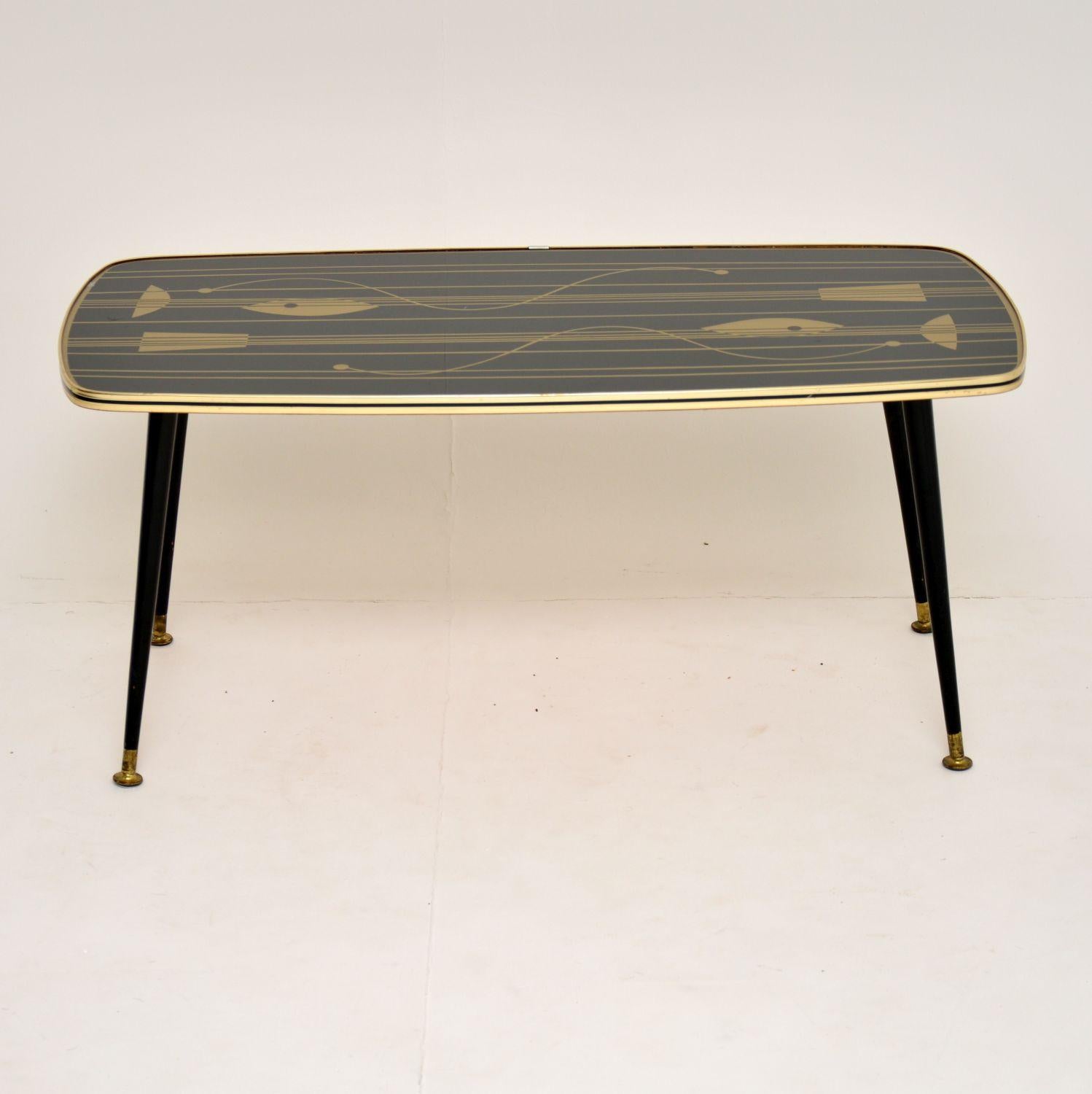 A beautifully designed vintage coffee table, this dates from the 1950s-1960s. It has a glass covered Formica top with amazing patterns, it sits on ebonized wooden legs with brass feet caps. This is in great condition for its age, with just some