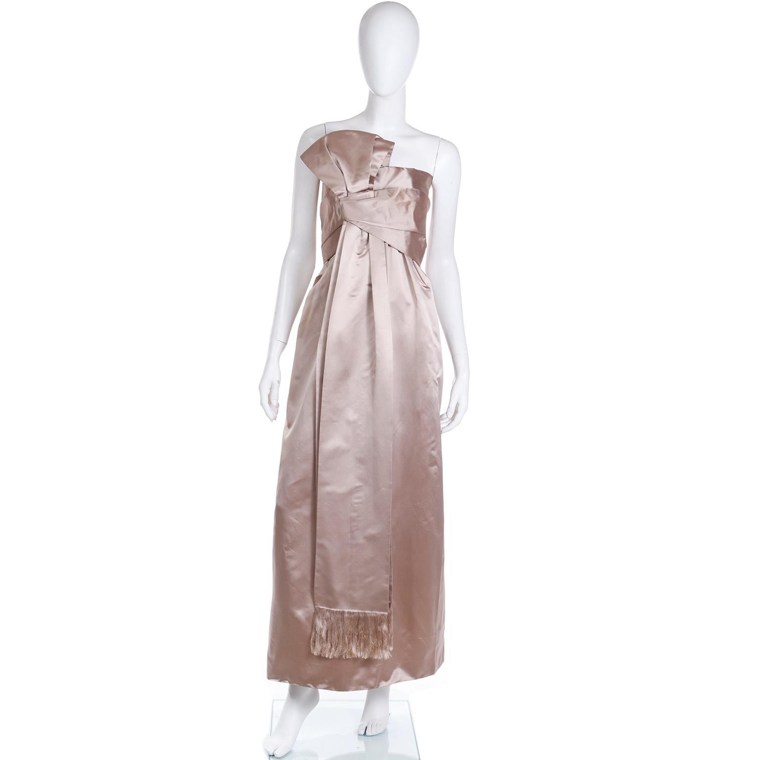 We are so happy to be able to offer this very rare, vintage 1950's strapless evening gown from Christian Dior in a pale taupe silk satin. This incredible dress has lovely tucks and gathers and a fringed sash that loops into a bow and the bodice and
