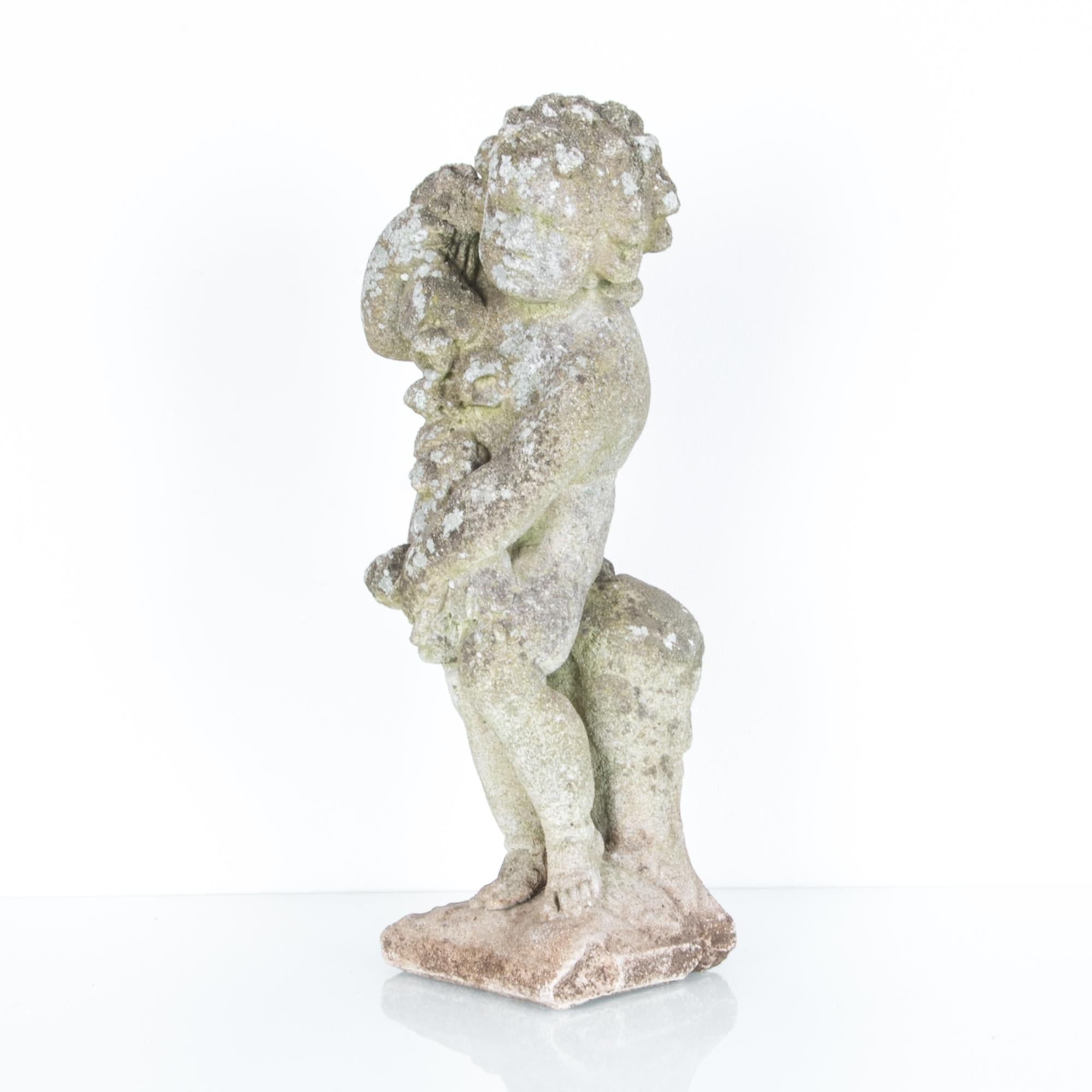 This concrete cherub statue was made in France, circa 1950. It holds a garland of flowers over its shoulder, a symbol of fertility. The grain of the statue is weathered and dappled with lichen, giving a nostalgic softness to the cherub’s expression.