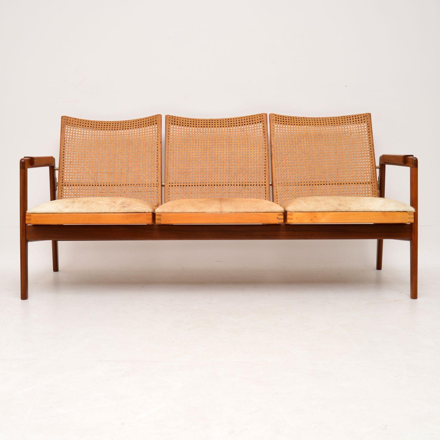 A stunning and very rare sofa made in Holland in the 1950s, this was designed by P.J Muntendam for Gebroeders Jonkers. It has a solid Afromosia frame, cane rattan back and amazing cow hide upholstery on the seats. The condition is superb for its
