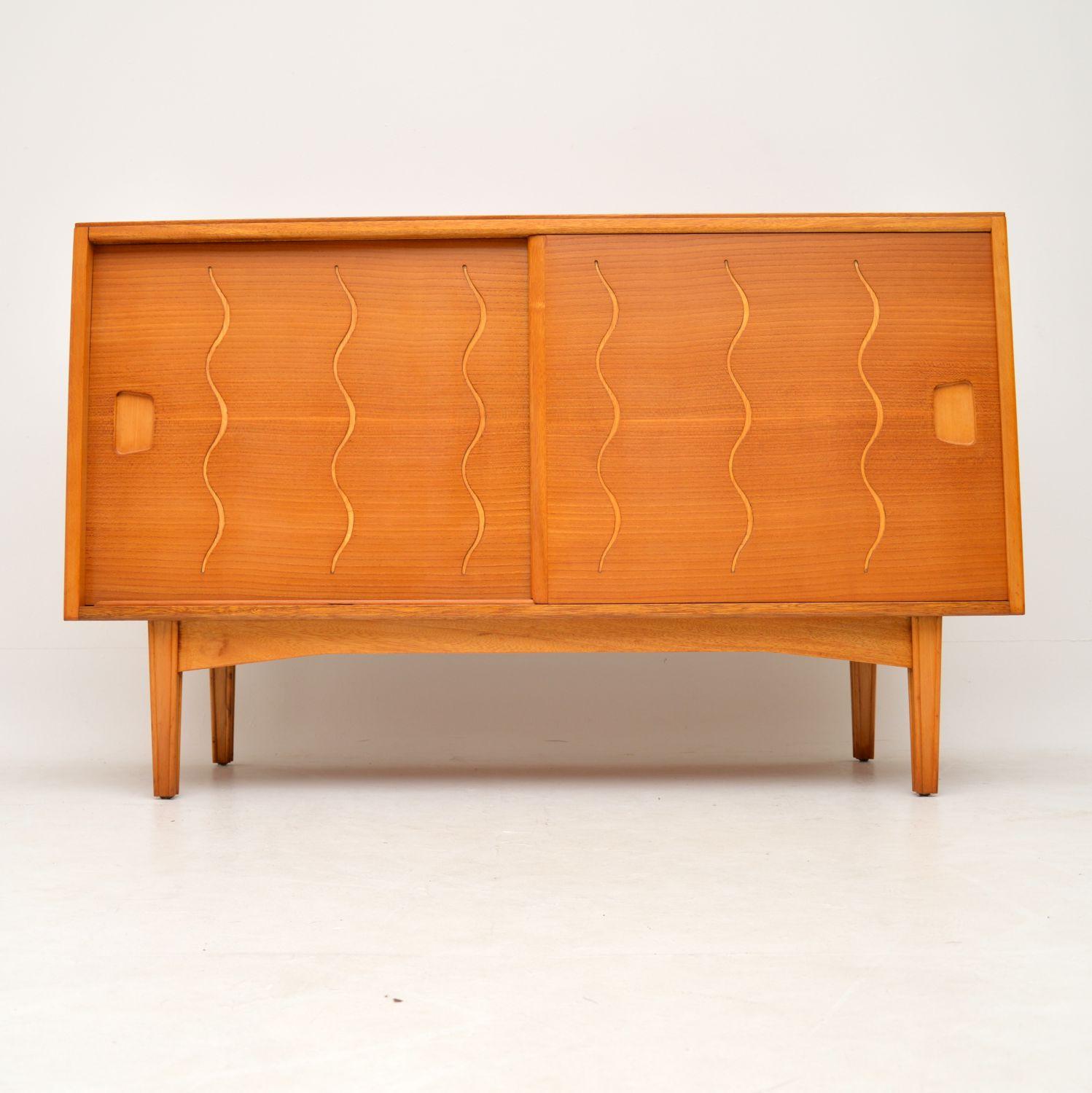 A stunning and very unusual vintage sideboard, this has a walnut carcass, elm sliding doors and lovely grooved etched patterns on the doors. The front is also angled at a slight slope, giving this an even more interesting design. This is British,