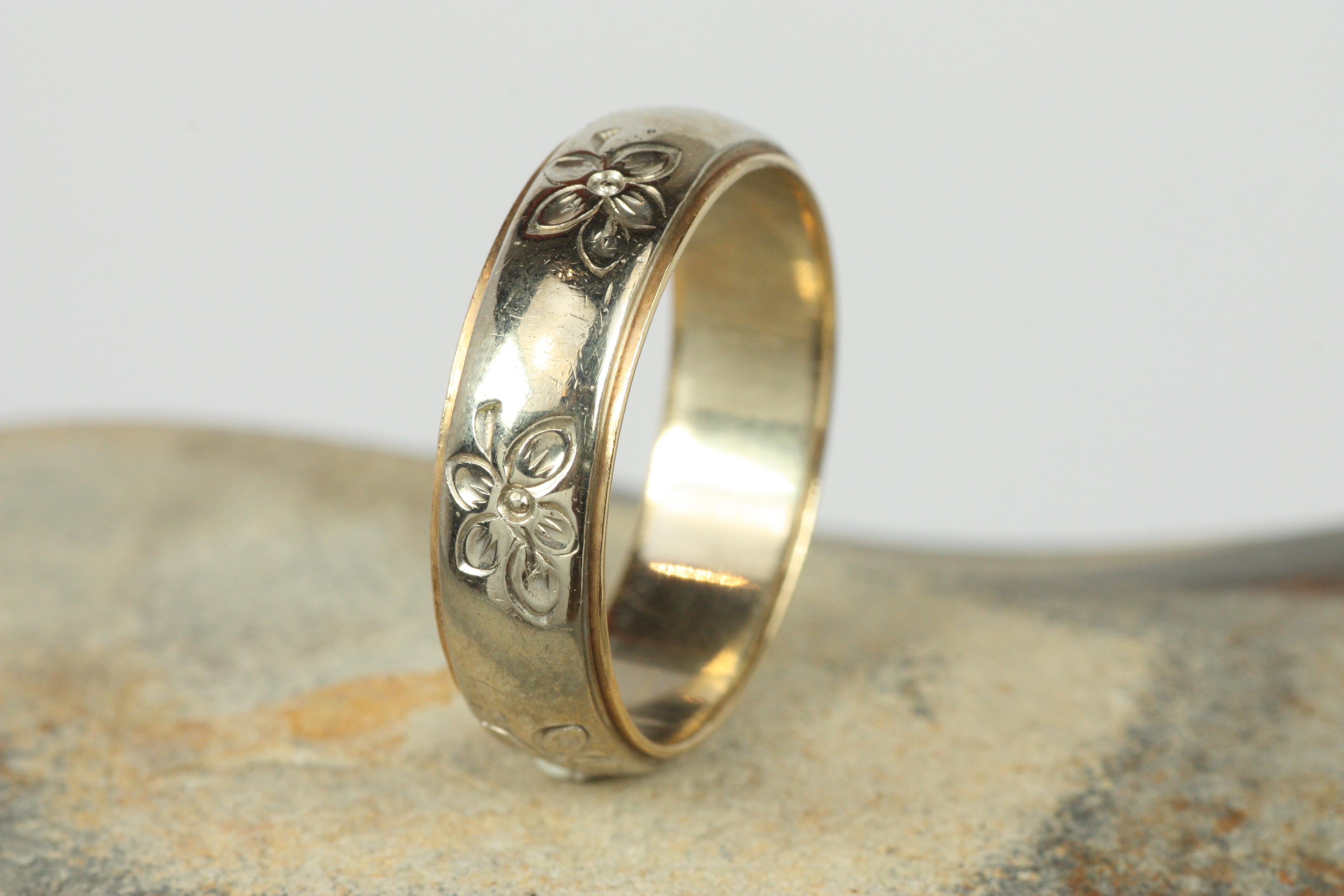 This 1950s vintage two-tone wedding band is one of many unique finds from our estate wedding ring collection at Bracken Jewelers in Santa Monica, California. The center of the ring is white gold and features a spaced, repeating embossed floral