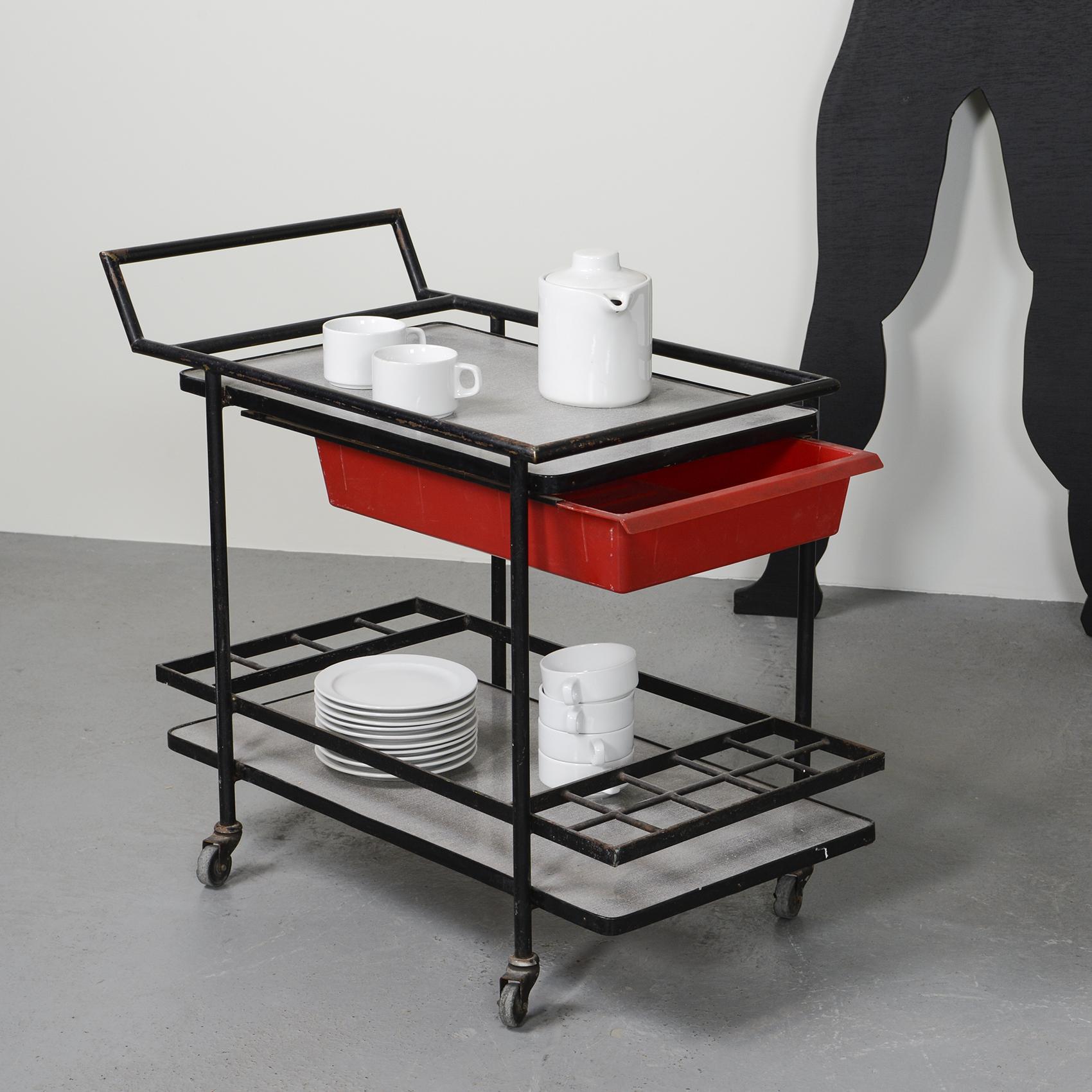 Trolley with two levels, square tubular structure in black lacquered metal with bottle compartments on the bottom shelf and a drawer in red moulded plastic by Charlotte Perriand.

The drawer is marked Modèle de Charlotte PERRIAND Breveté S.G.D.G.