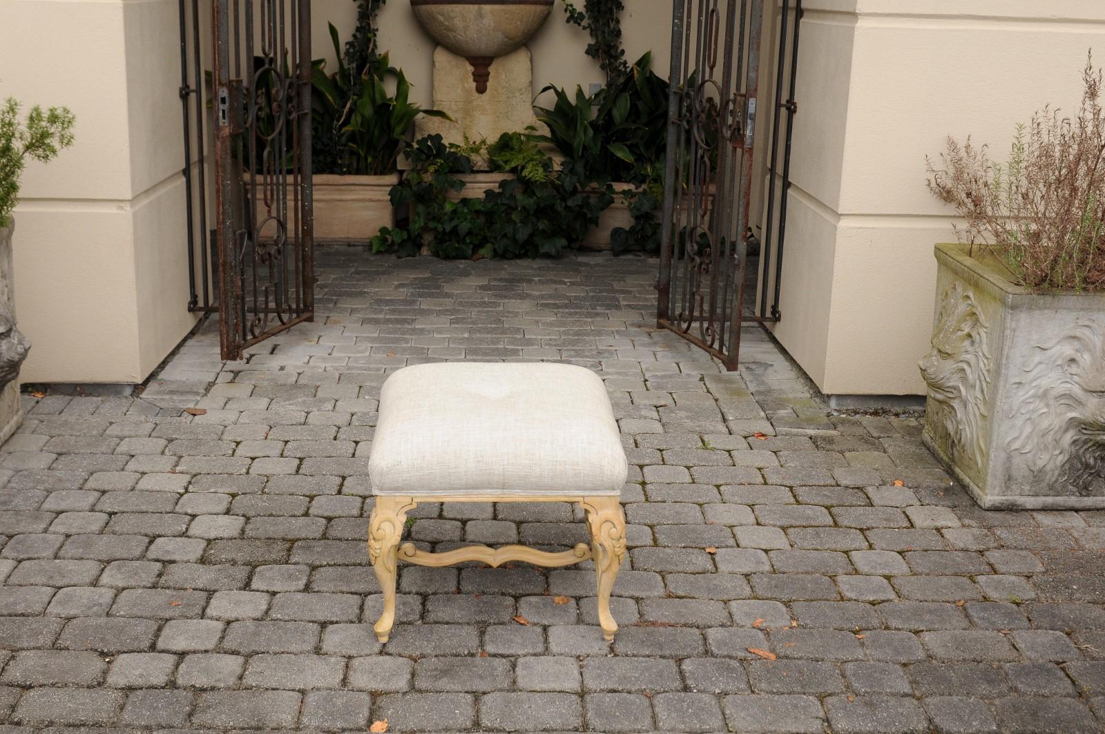 An Italian vintage Rococo style pinewood ottoman from the mid-20th century, with cabriole legs, cross stretcher and new linen upholstery. Born during the midcentury period, this exquisite Italian ottoman / stool features a square shaped seat,