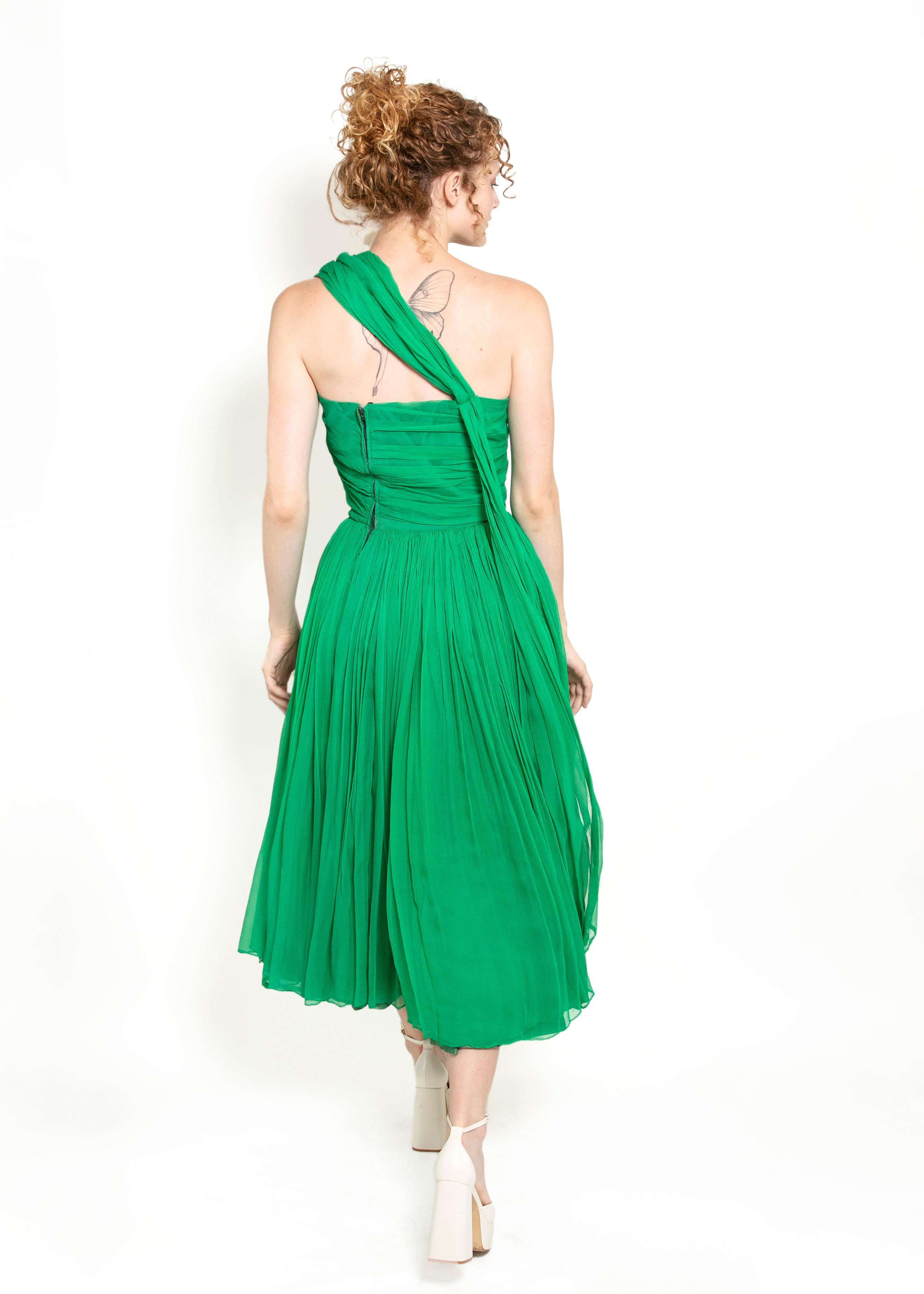 Dieses atemberaubende 1950's Vintage Kelly Green Silk Chiffon Cocktailkleid ist der perfekte Weg, um bei jedem besonderen Anlass aufzufallen. Der luxuriöse und zeitlose Seidenchiffon-Stoff sorgt für einen Drapierungseffekt, während der Faux Shawl