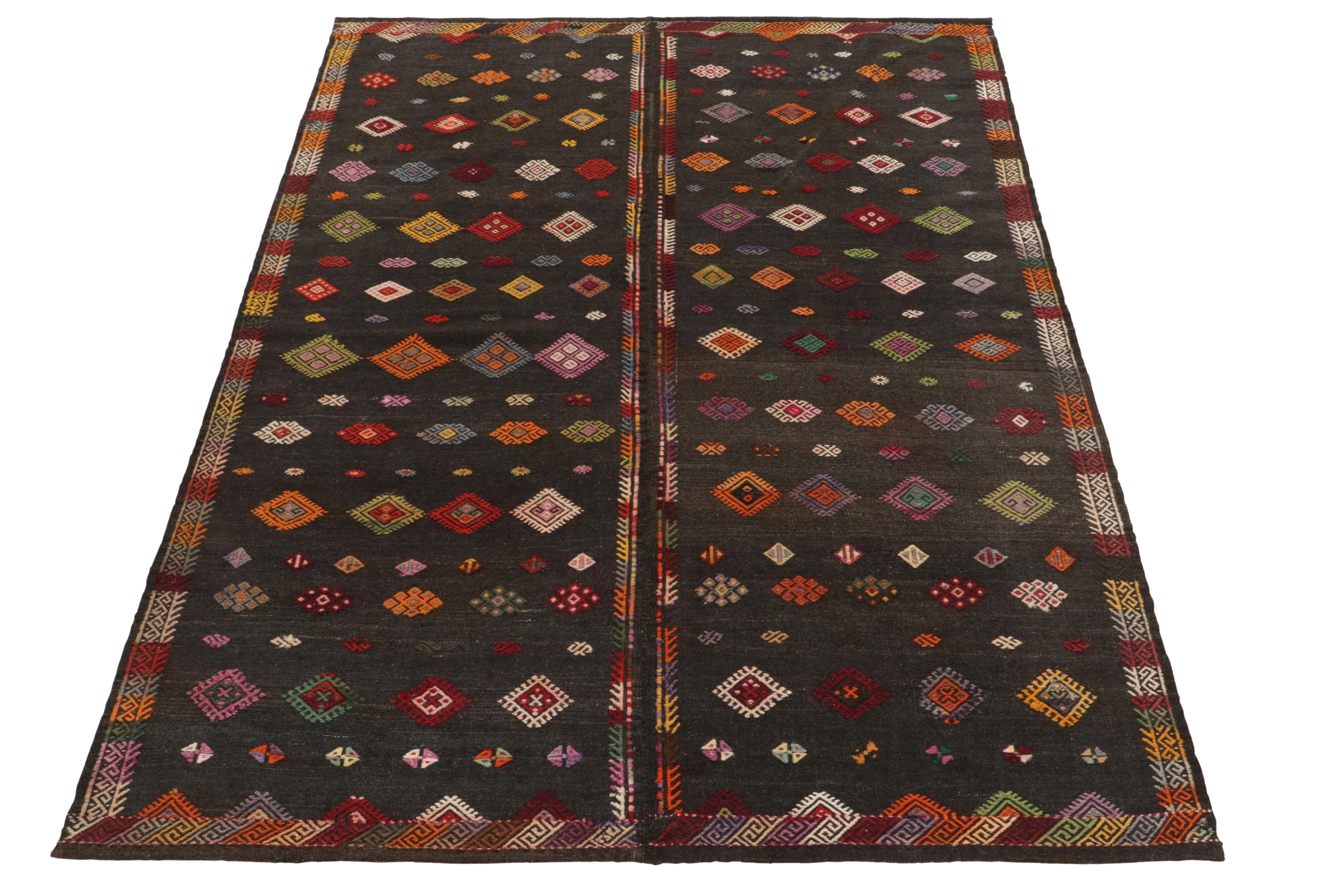 Handwoven in wool, a 7x9 vintage kilim rug from Turkey connoting distinguished mid-century aesthetics. The earth tonal gray-black background naturally uplifts brilliant embroidered patterns in variegated tones for an alluring visual appeal.