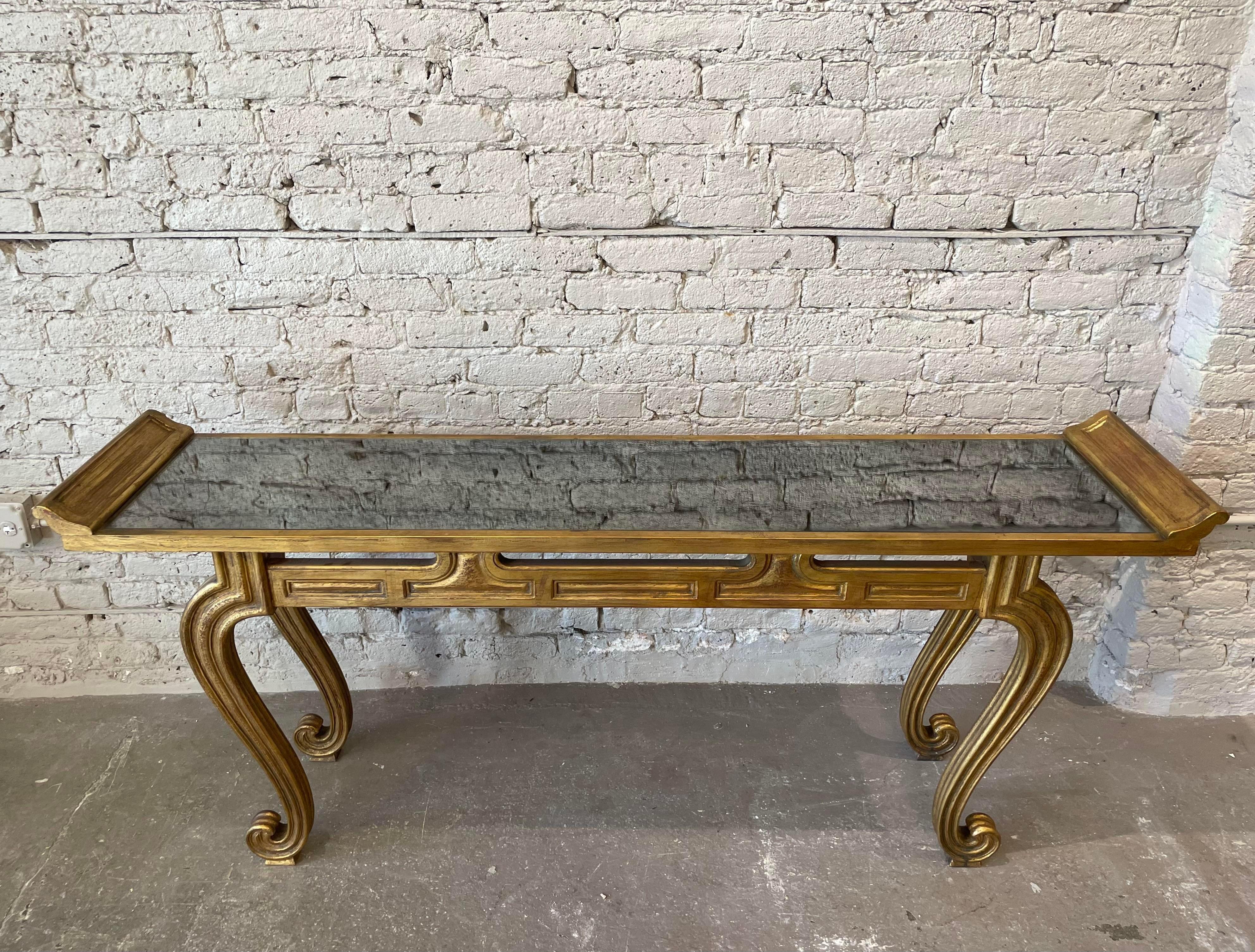 This console table is a 1950s interpretation of the altar tables traditionally found in Chinese reception halls. The gilt-painted wood frame features the typical everted flanges and scrolled legs; the table surface is gold-specked mirror. The height