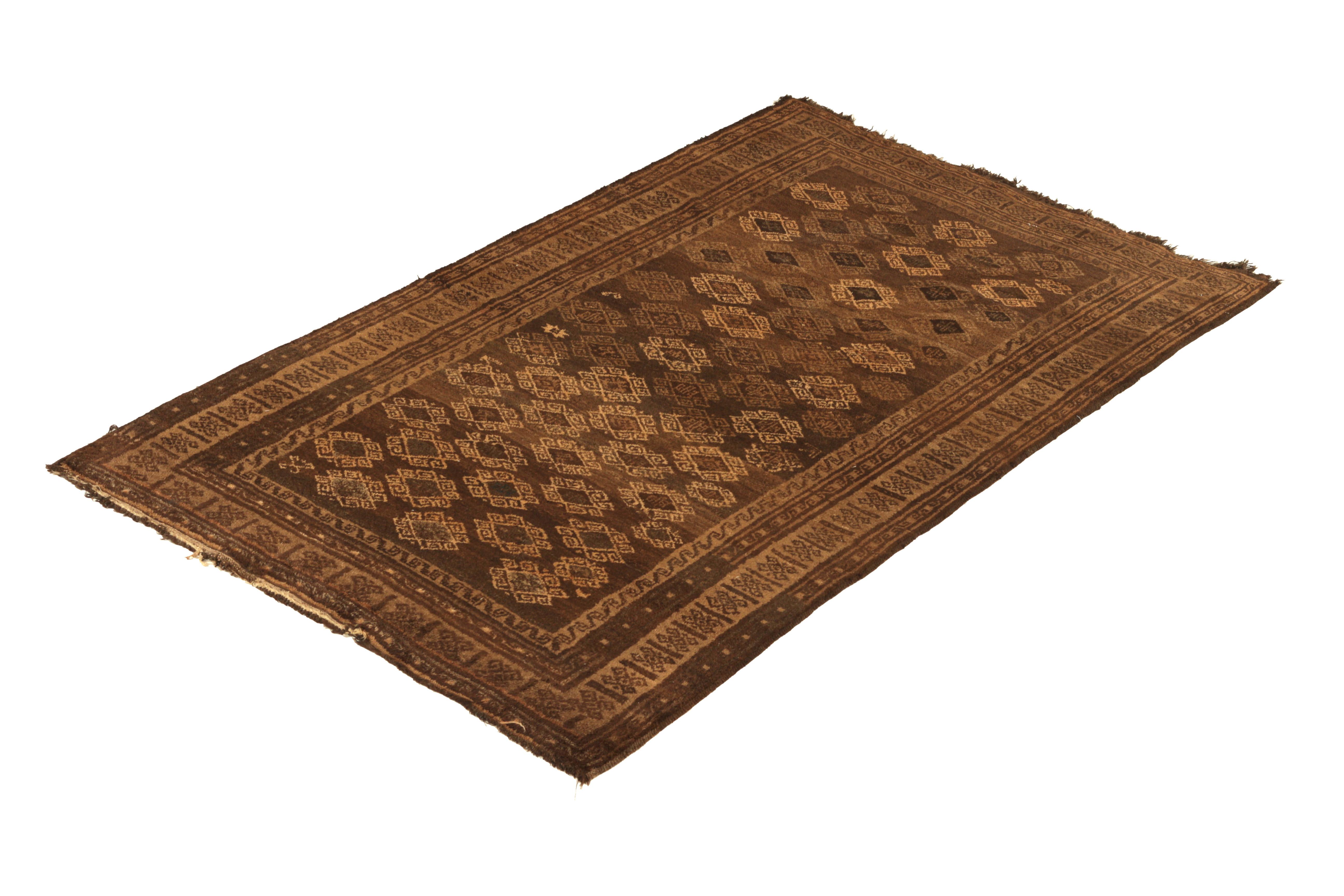 Hand knotted in wool originating from Persia circa 1950-1960, this vintage rug connotes a midcentury Baluch tribal rug design, marrying the Classic richness of beige-brown hues with the equally celebrated variations of ram’s horn motifs in the