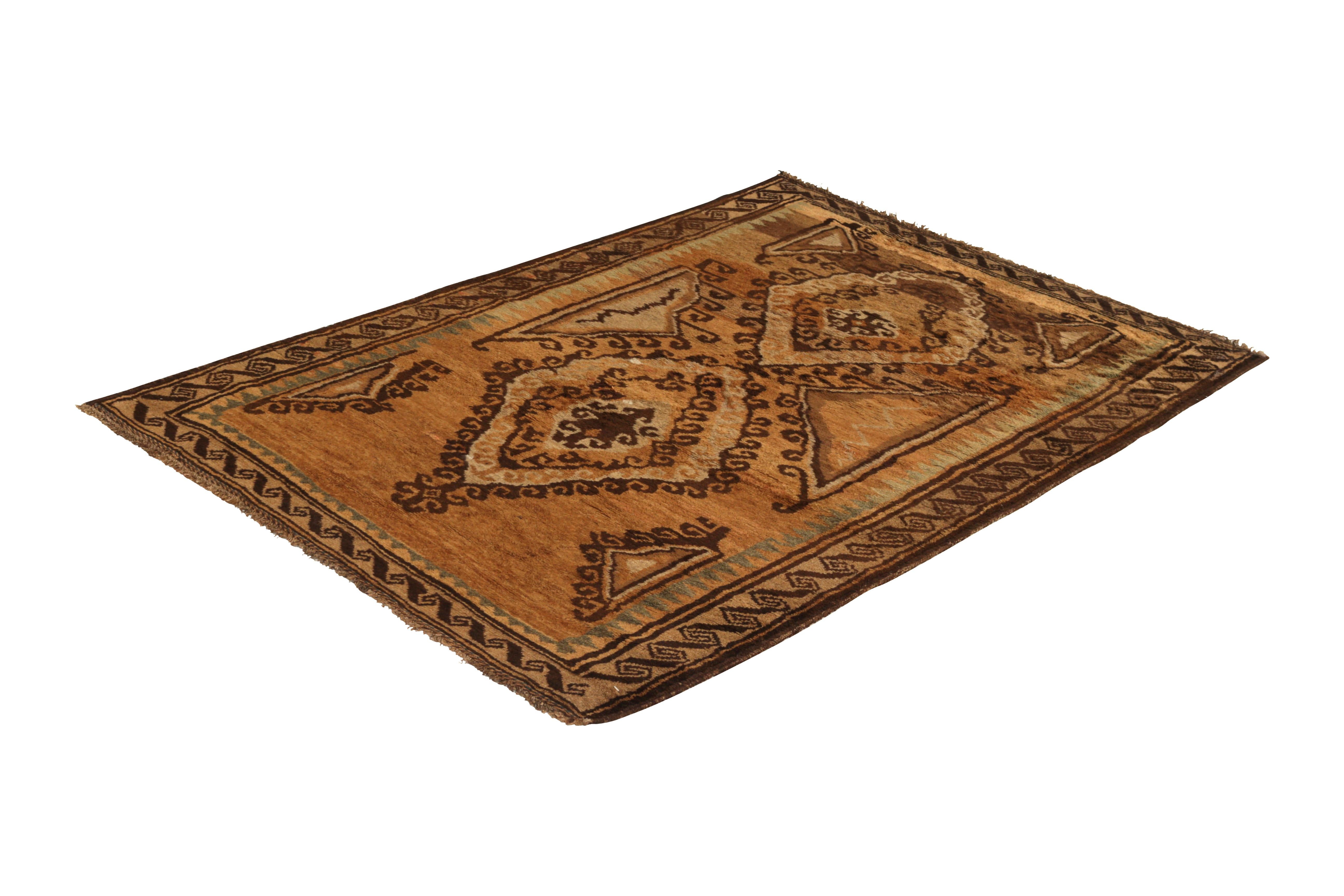 Hand knotted in wool originating from Persia circa 1950-1960, this vintage rug connotes a midcentury Baluch tribal rug design, marrying the Classic richness of beige-brown hues with the equally celebrated tribal medallion patterns in the central