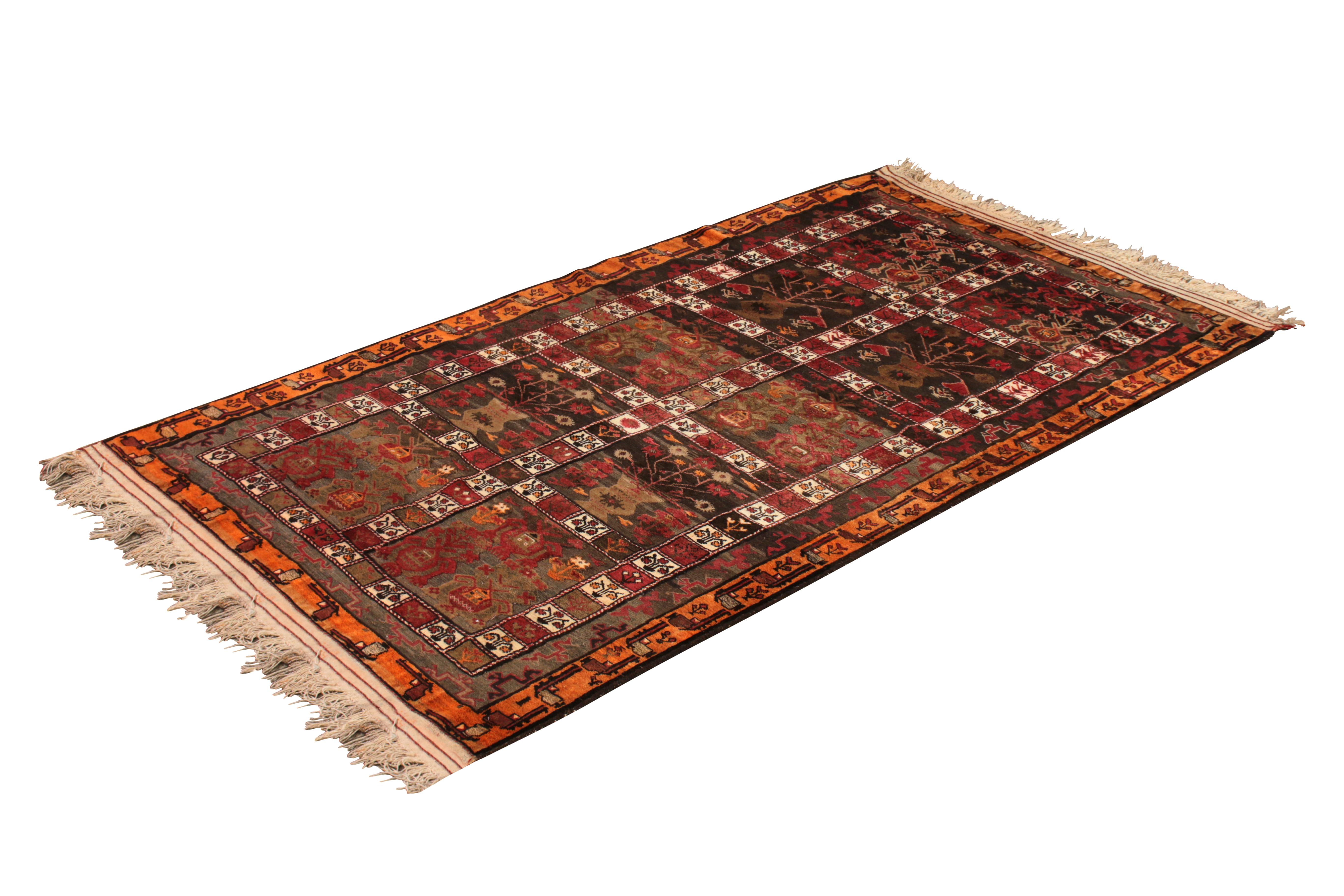 Handwoven in wool originating from Afghanistan, circa 1950-1960, this vintage Kilim connotes a midcentury adaptation of a vase floral pattern in a distinctly rich burgundy and crimson red colorway, playing naturally into earth tones of brown